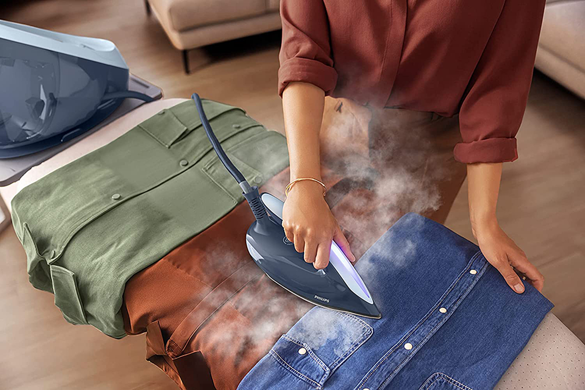 Una persona che stira una camicia di jeans blu su un'asse da stiro con altre camicie.