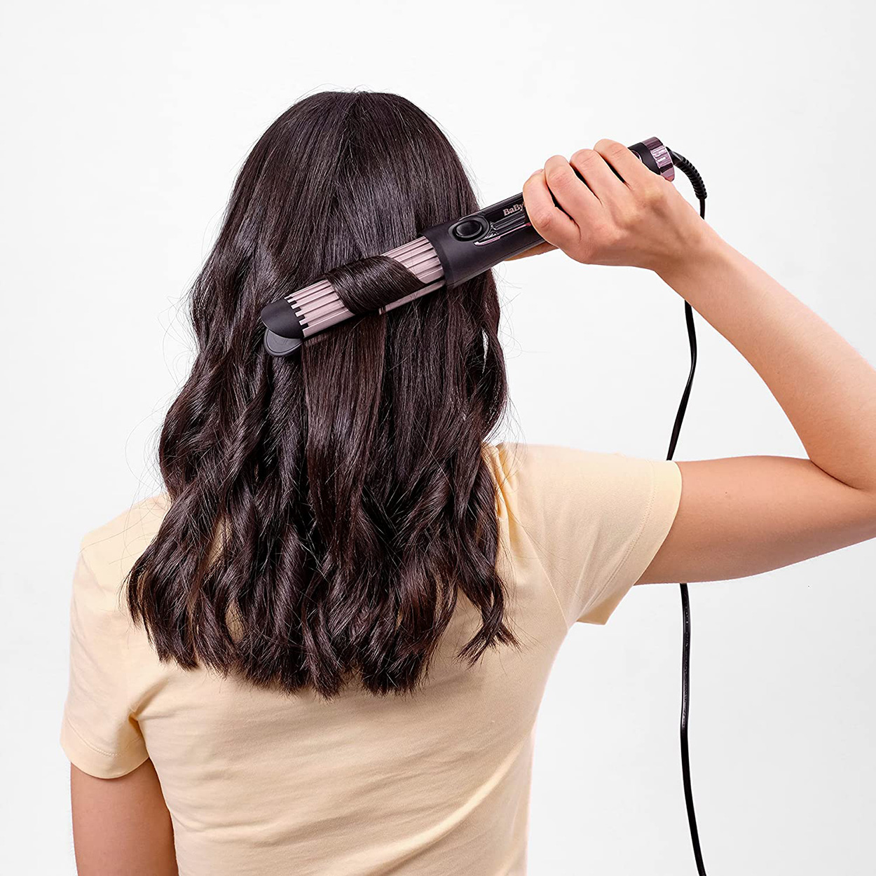 Frau, die ihre Haare mit einem Glätteisen stylt. Sie ist von der Kamera abgewandt.