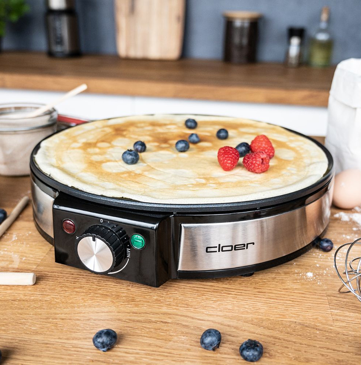 Maszyna do naleśników z naleśnikiem i jagodami. Składniki na drewnianym stole. Czarne i srebrne urządzenie.