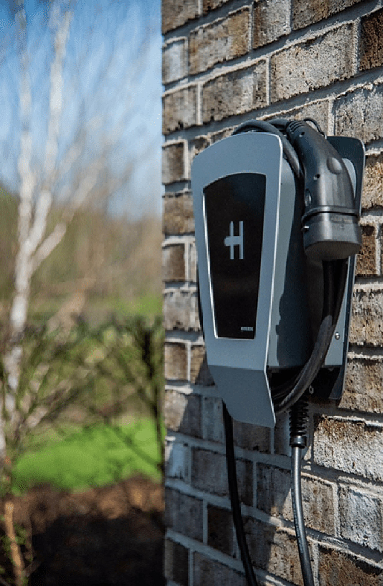 Une borne de recharge pour véhicules électriques montée sur un mur de briques à l'extérieur, avec câble.