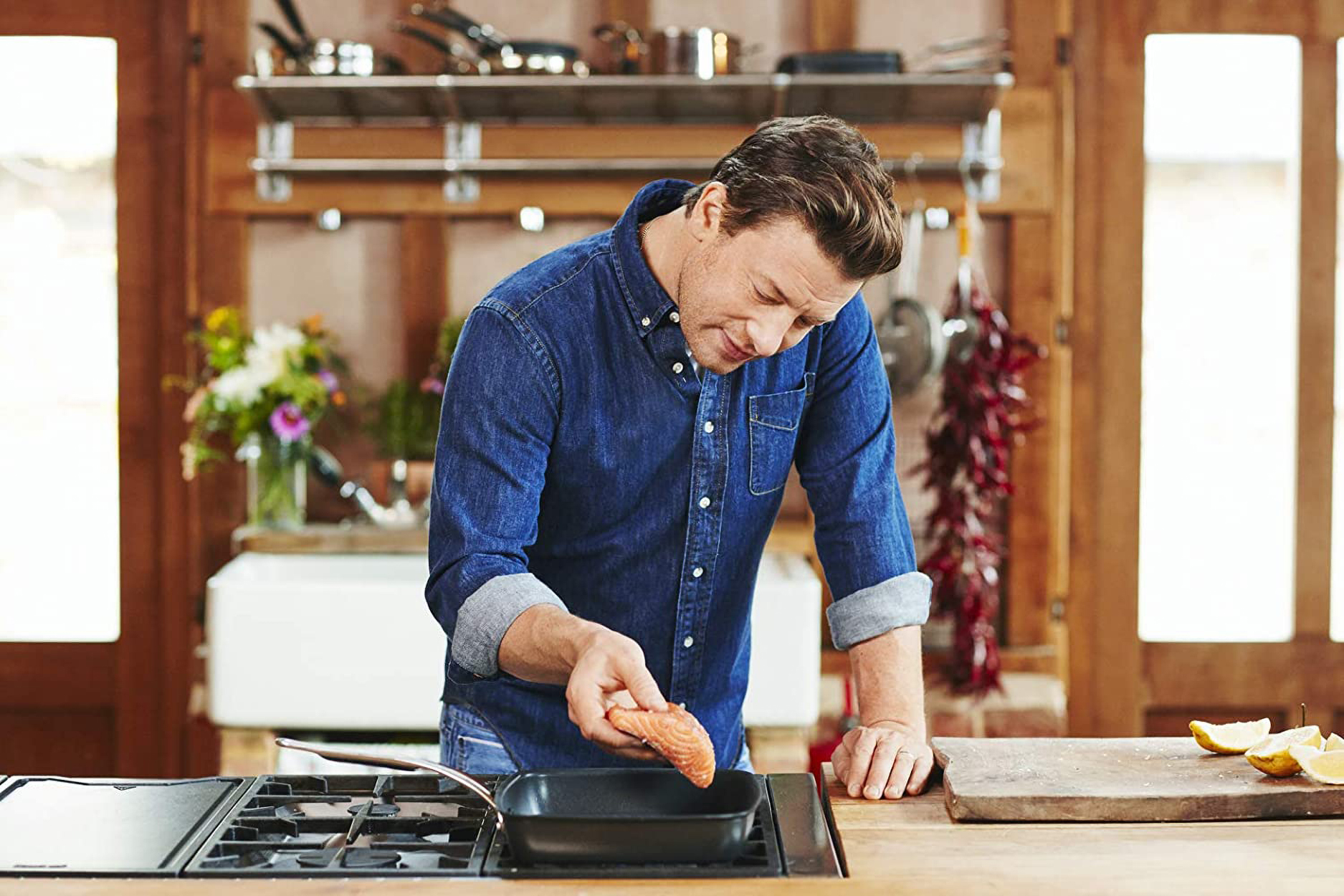 Koch in Jeanshemd legt Lachsfilet in eine Pfanne auf dem Herd in einer Küche.