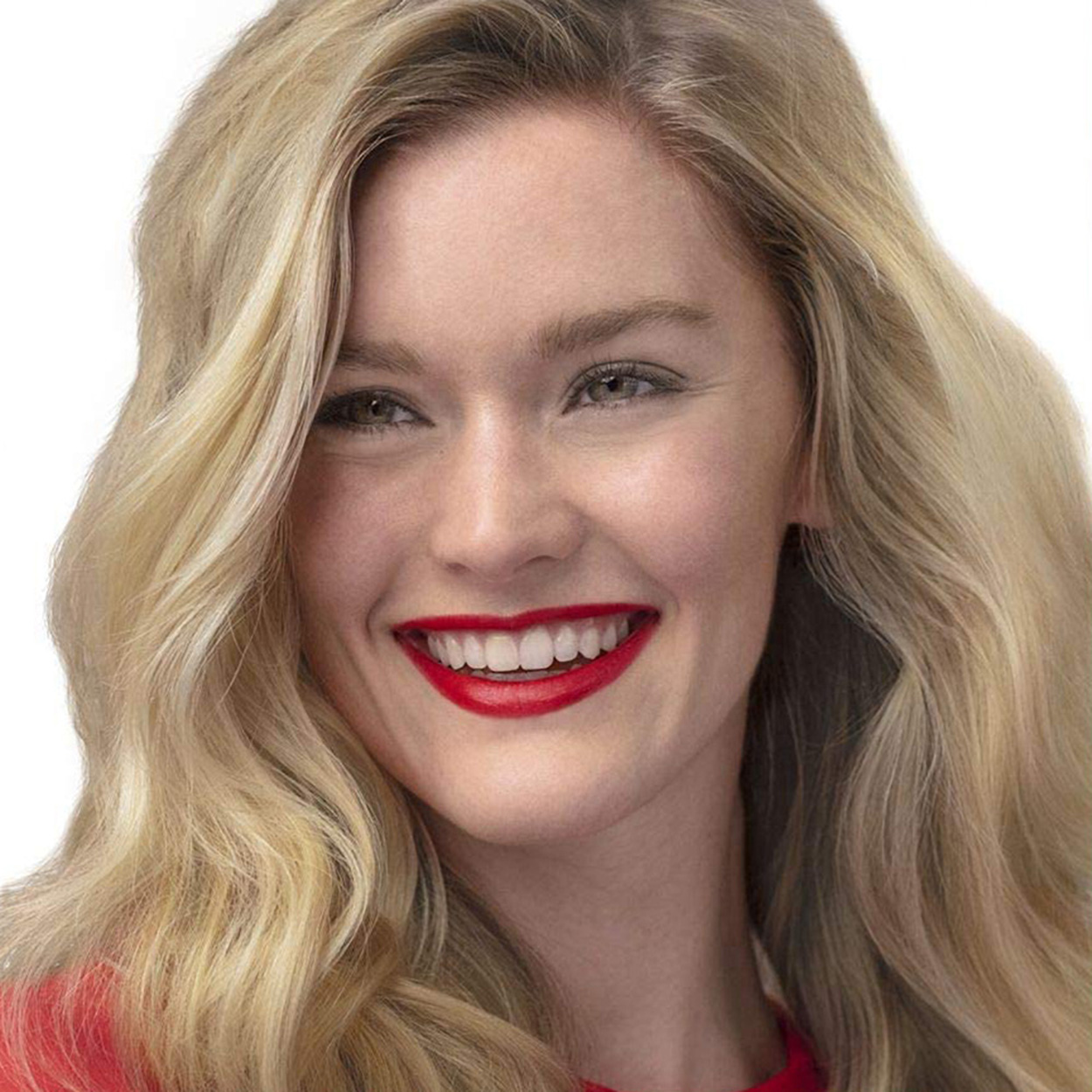 Donna bionda con rossetto rosso sorridente, guarda la fotocamera con occhi luminosi.