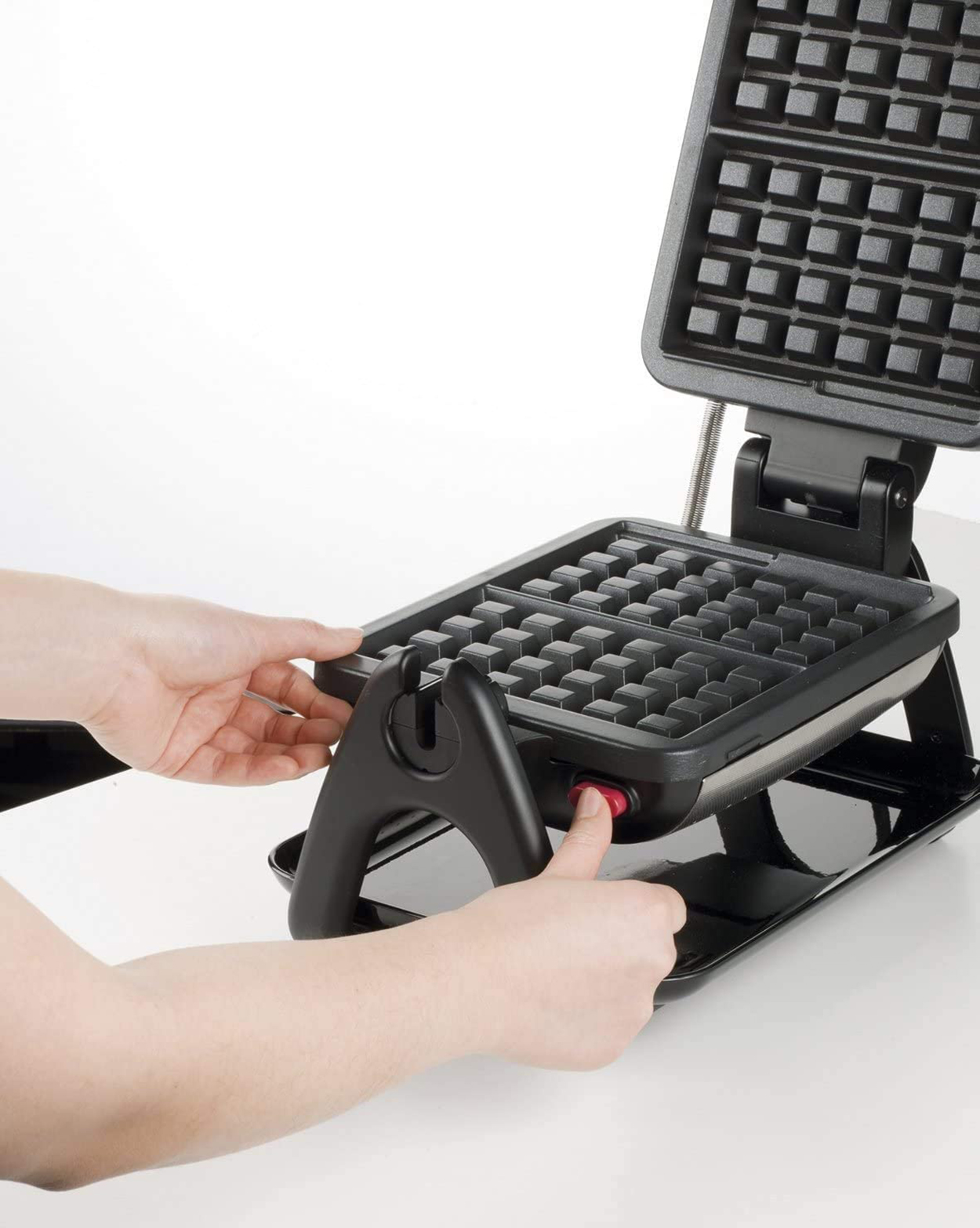 Ręce osoby naciskającej przycisk czarnej gofrownicy. Górna część jest otwarta.