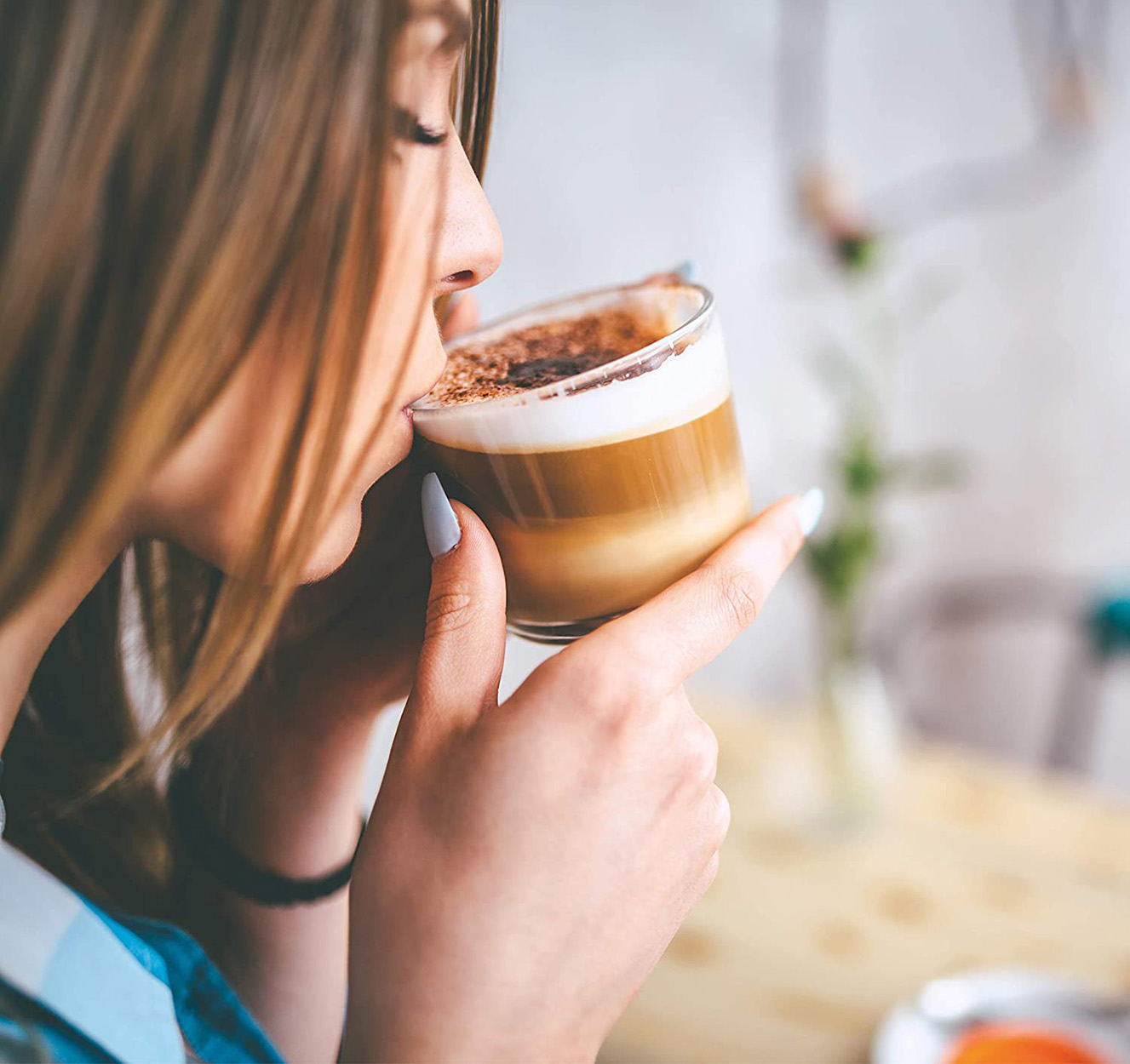 Eine Frau, die einen Cappuccino aus einem Glasbecher trinkt, Nahaufnahme von Gesicht und Händen.