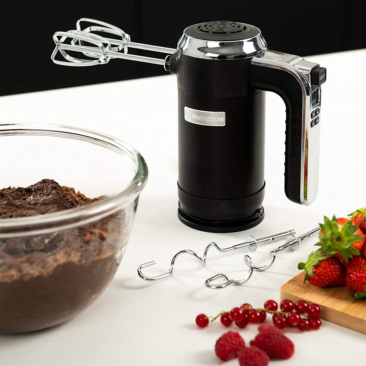 Schwarzer Handmixer mit Chromaufsatz. Schüssel mit Teig links und Erdbeeren rechts.