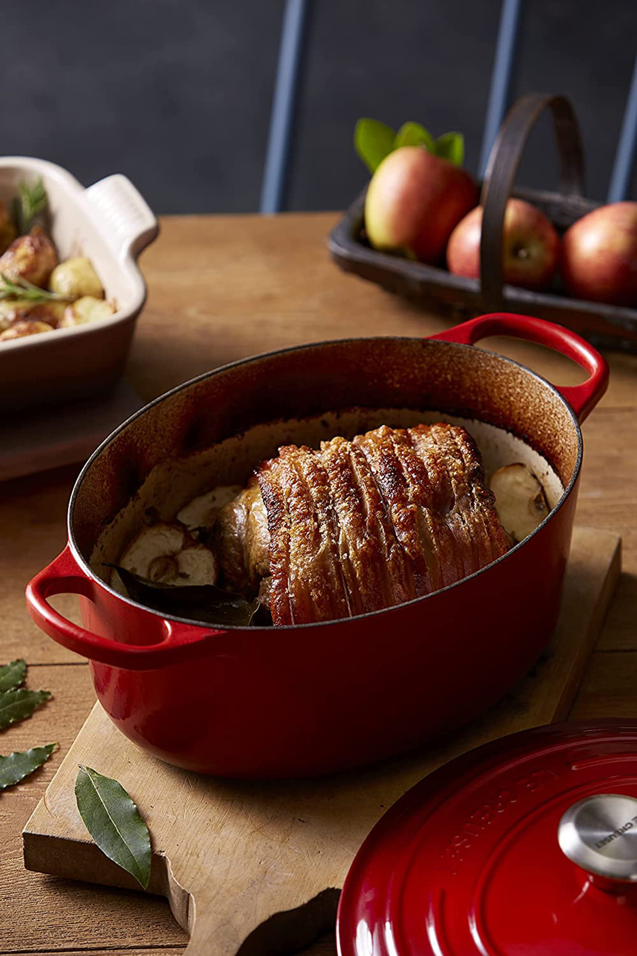 Un plat à casserole ovale rouge avec un plat de porc rôti à l'intérieur, sur une planche à découper en bois.