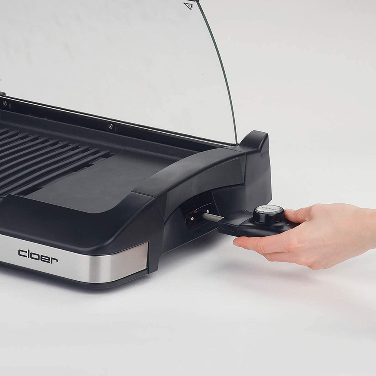 Elektrischer Grill mit Griff, der von einer Hand verstellt wird. Der Grill ist schwarz mit silberner Blende.