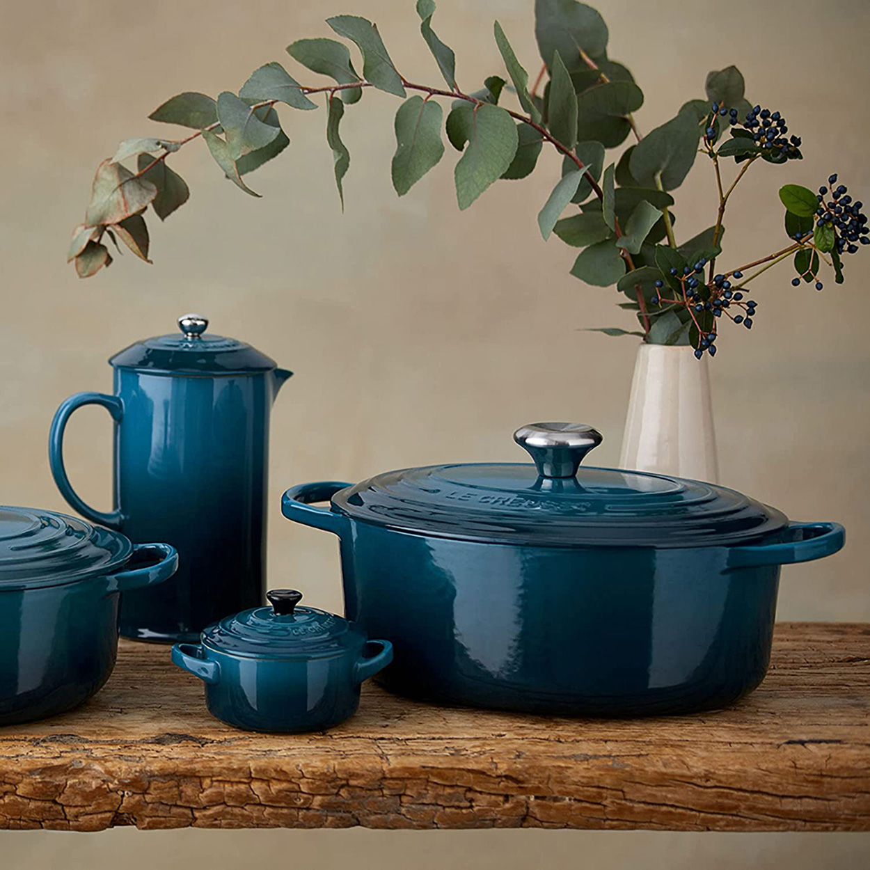 Türkisfarbenes Kochgeschirr-Set mit French Press und Vase mit Grünzeug. Holztisch-Hintergrund.