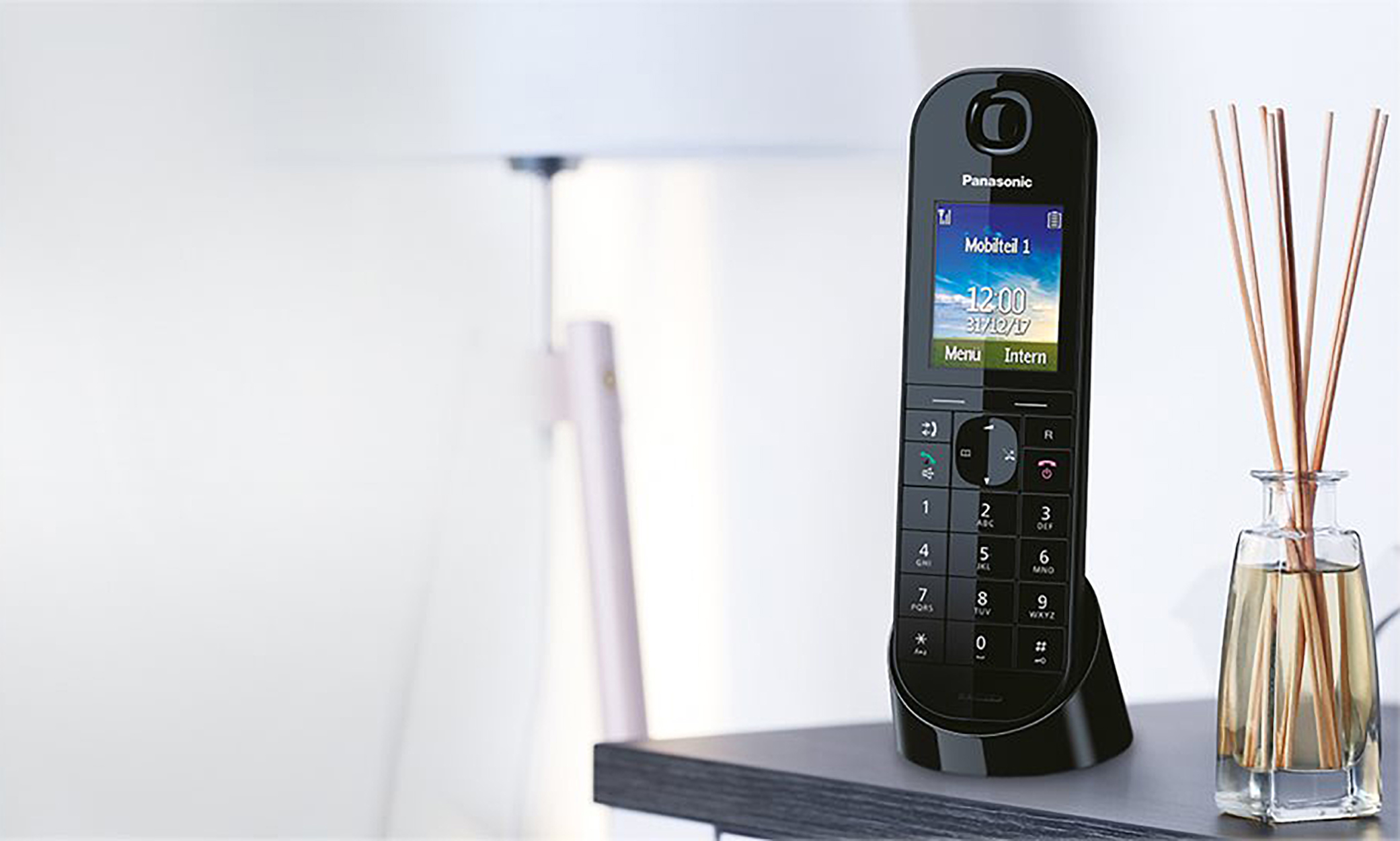 Schwarzes schnurloses Telefon auf einer Dockingstation. Vase mit Stöcken rechts.