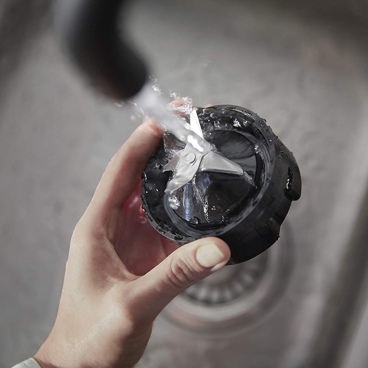 Eine Hand wäscht eine Mixer-Klinge unter fließendem Wasser in einem Waschbecken.