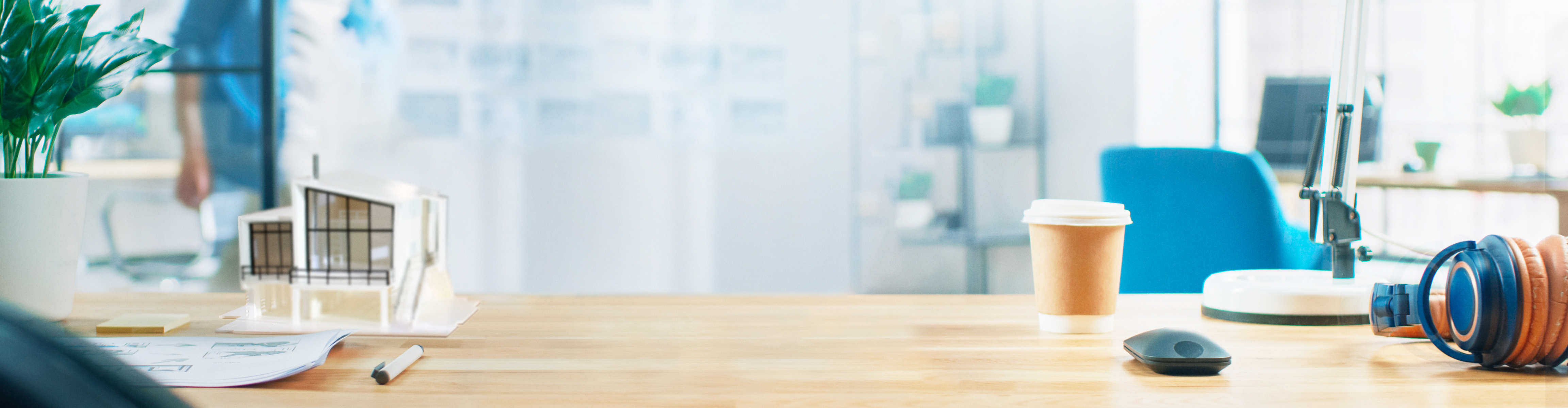 Biurko z modelem domu, słuchawkami, kubkiem kawy i myszą komputerową.