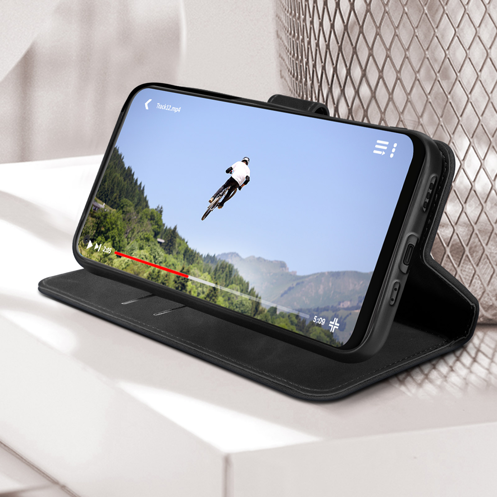 Telefono nero con video, custodia nera, su superficie bianca.