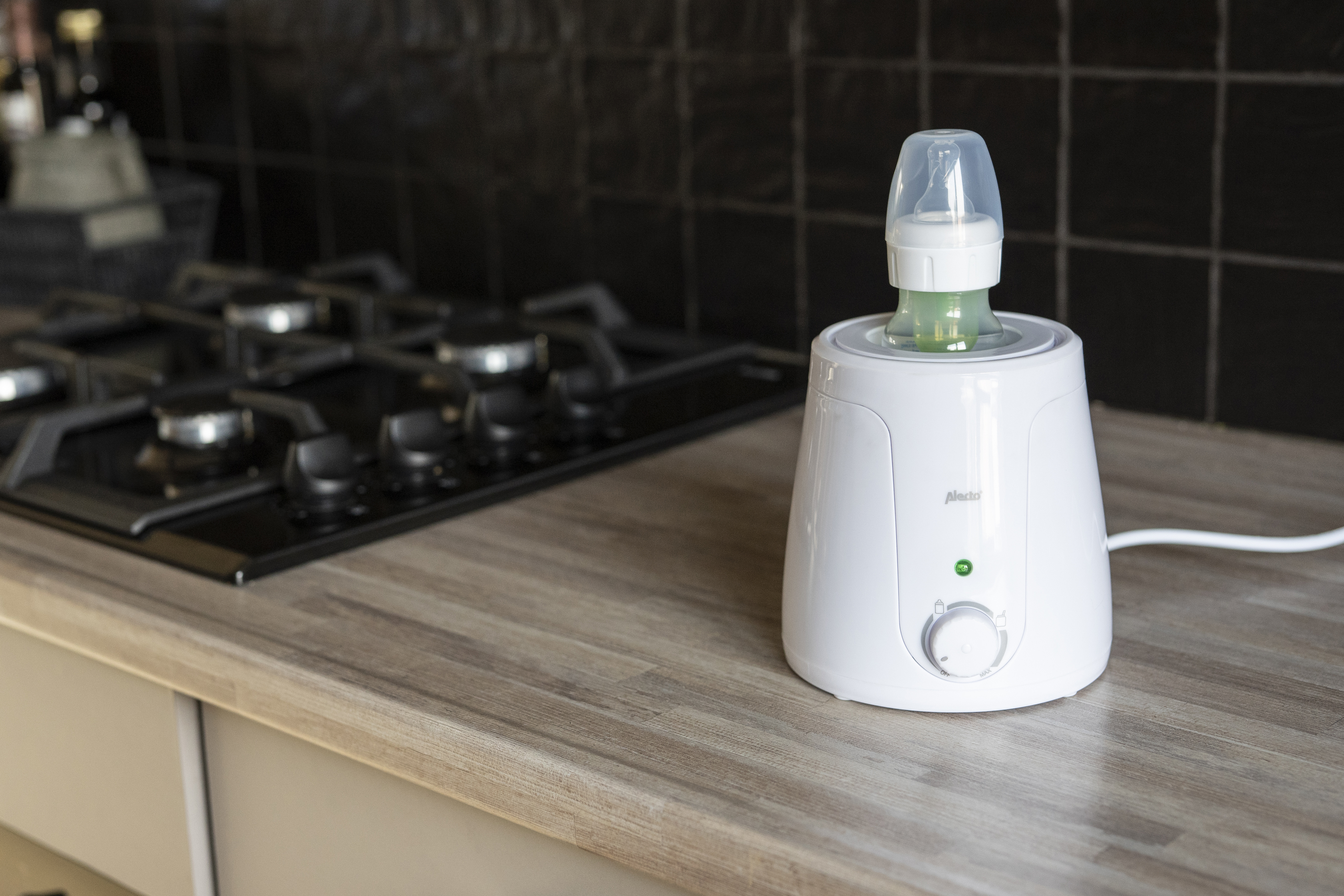 Biała podgrzewacz do butelek z butelką stoi na blacie obok kuchenki.