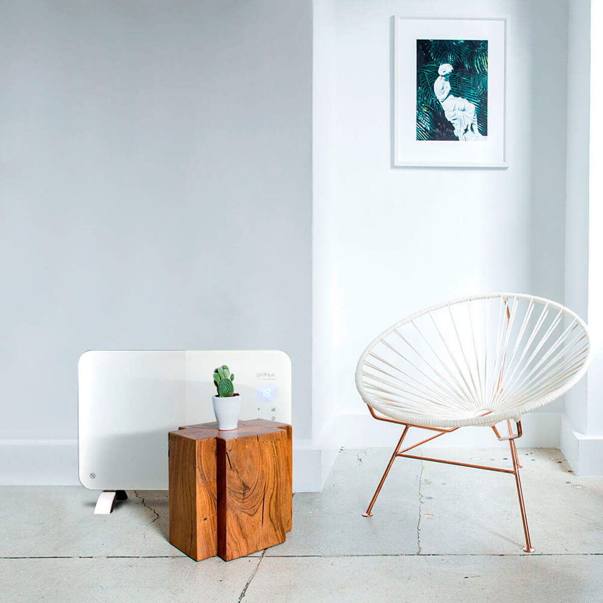 Escena de sala de estar con calefactor blanco, cactus, silla y arte en la pared.