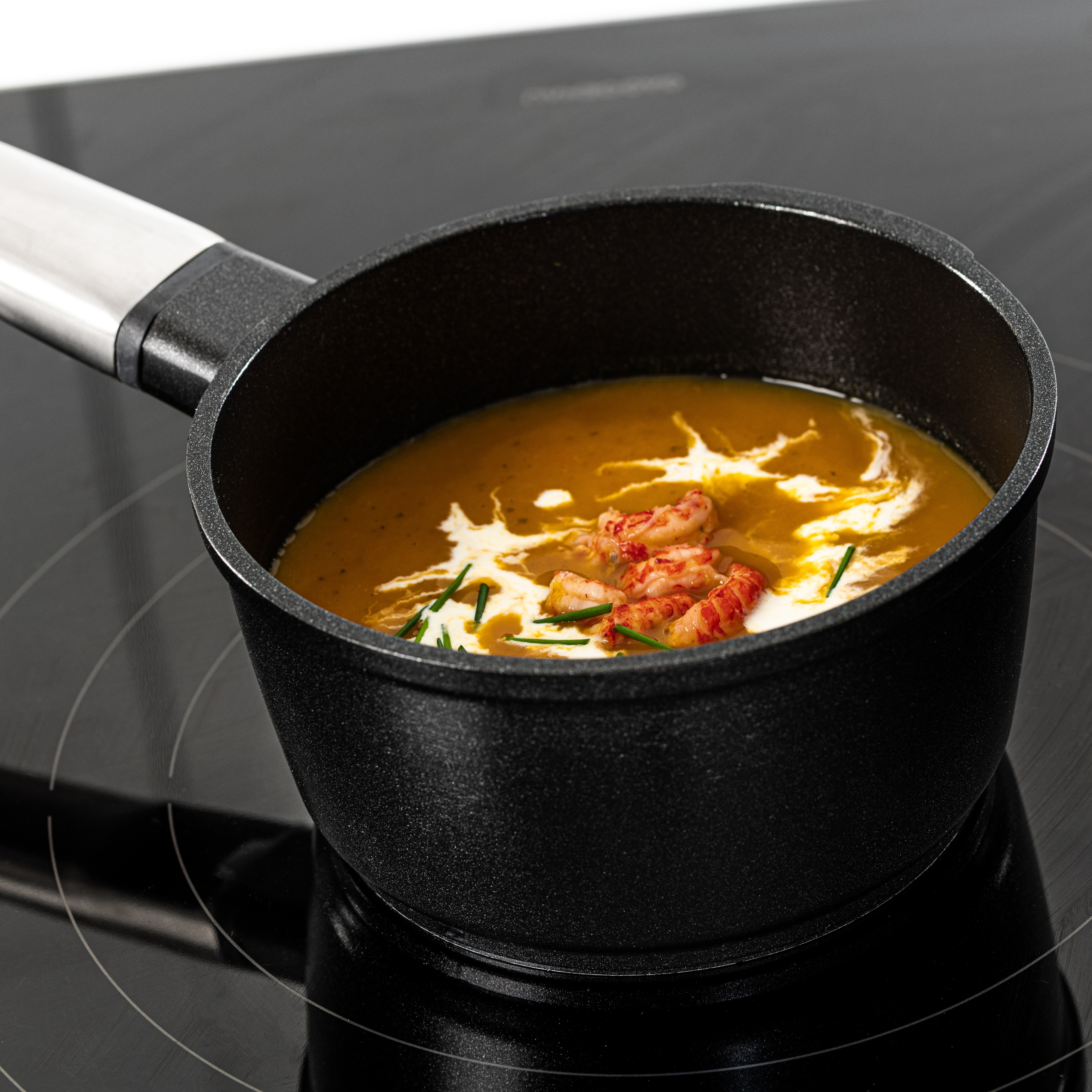 Schwarzer Kochtopf mit orangener Suppe, bedeckt mit Sahne, Schnittlauch und Krebsen auf einem schwarzen Herd.