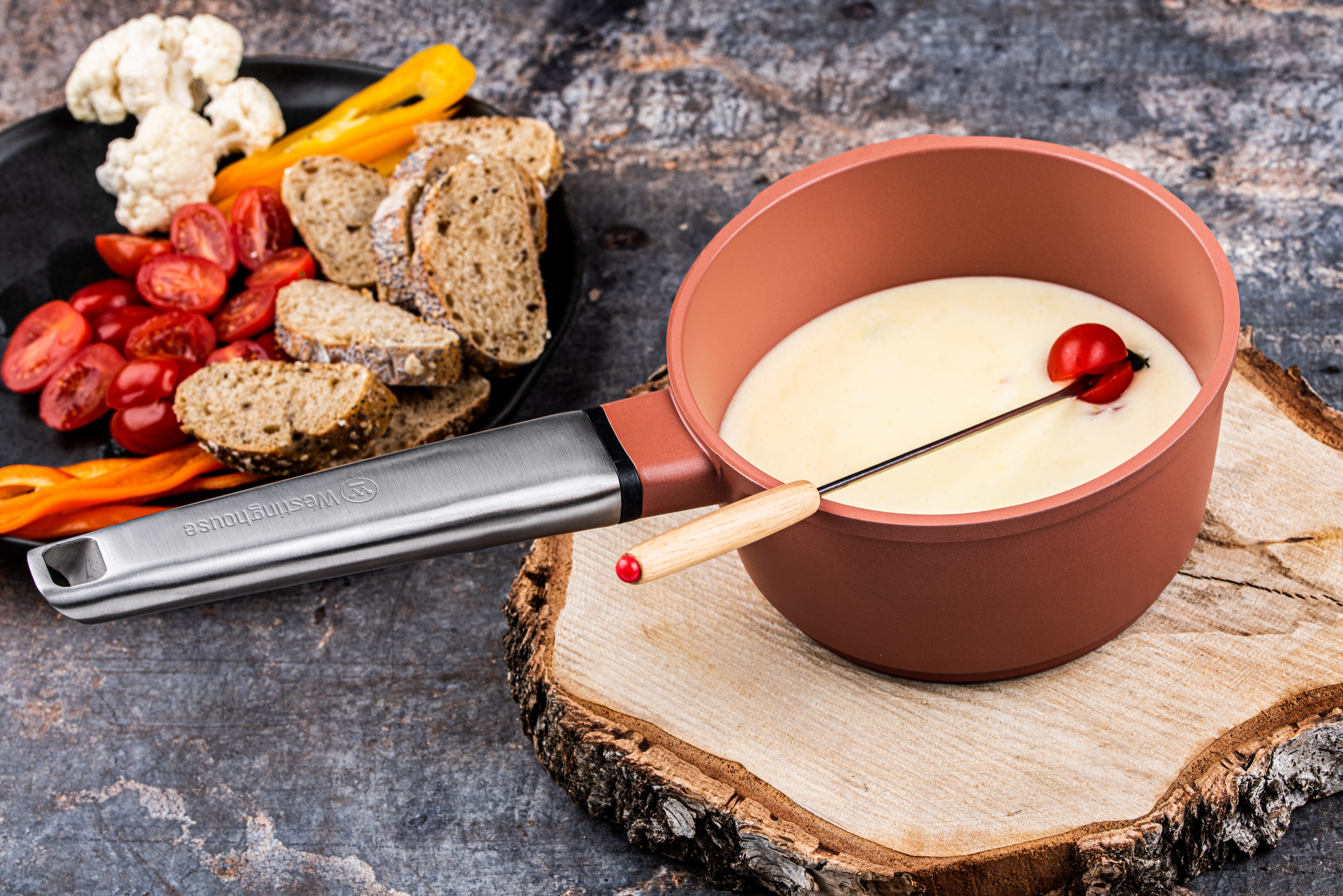 Fondue-Set mit Speisen, darunter Brot, Gemüse und eine Kirsche, auf Holzbasis.