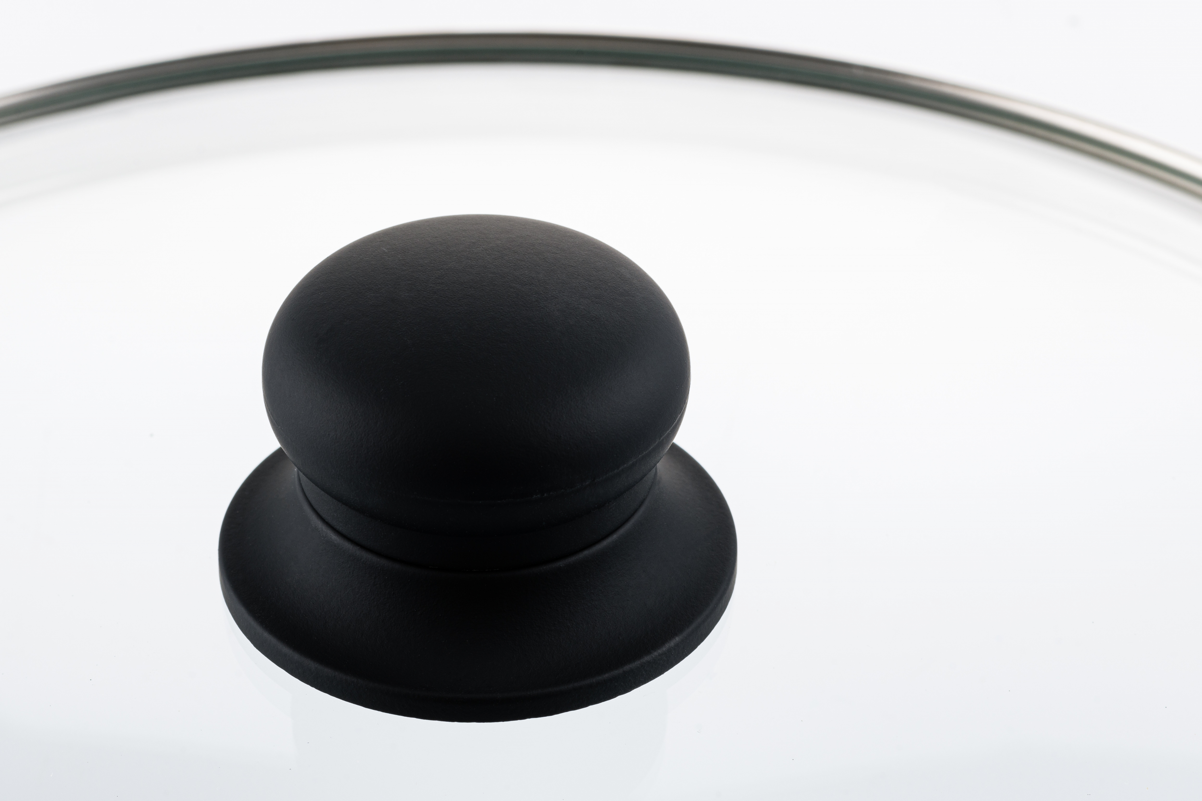 Ein schwarzer Knopf auf einem Glasdeckel, der Licht reflektiert, mit weißem Hintergrund.
