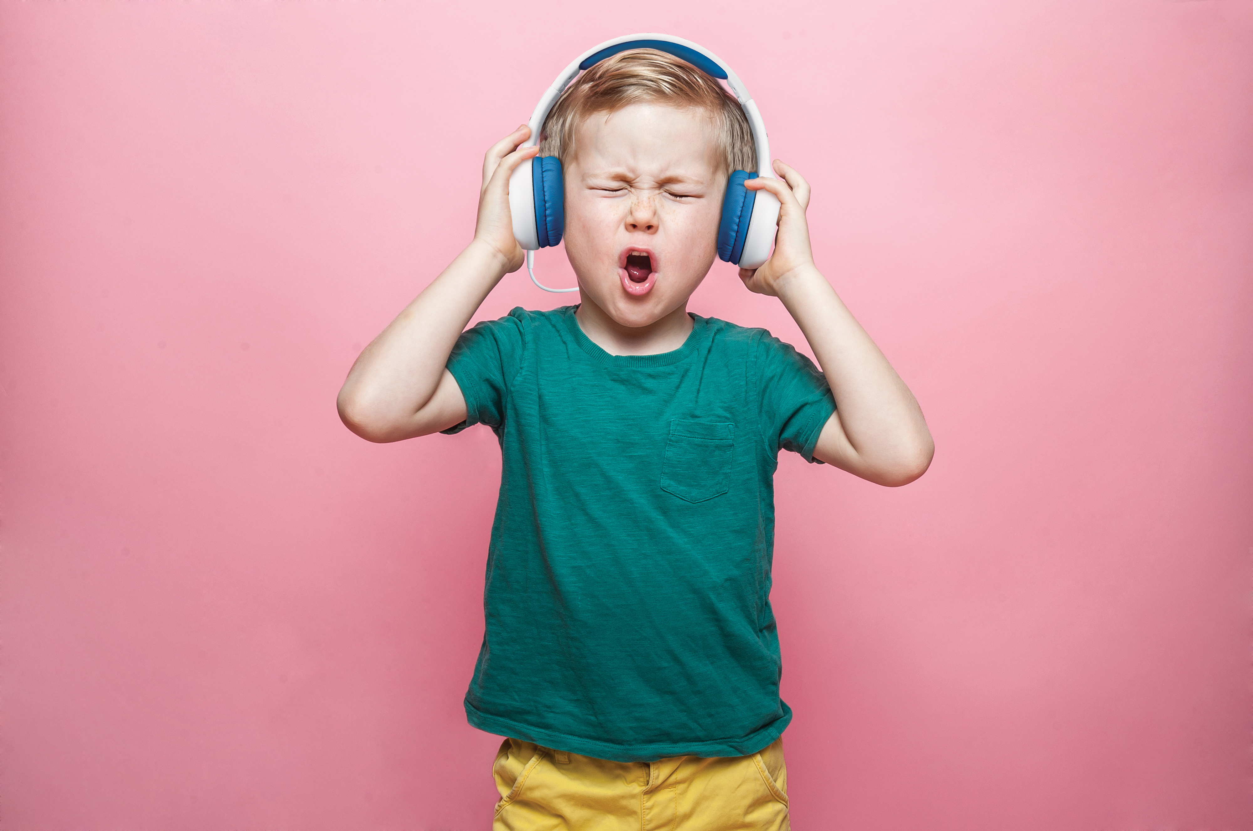 Mały chłopiec w słuchawkach krzyczy. Ma na sobie zieloną koszulkę i żółte spodenki.