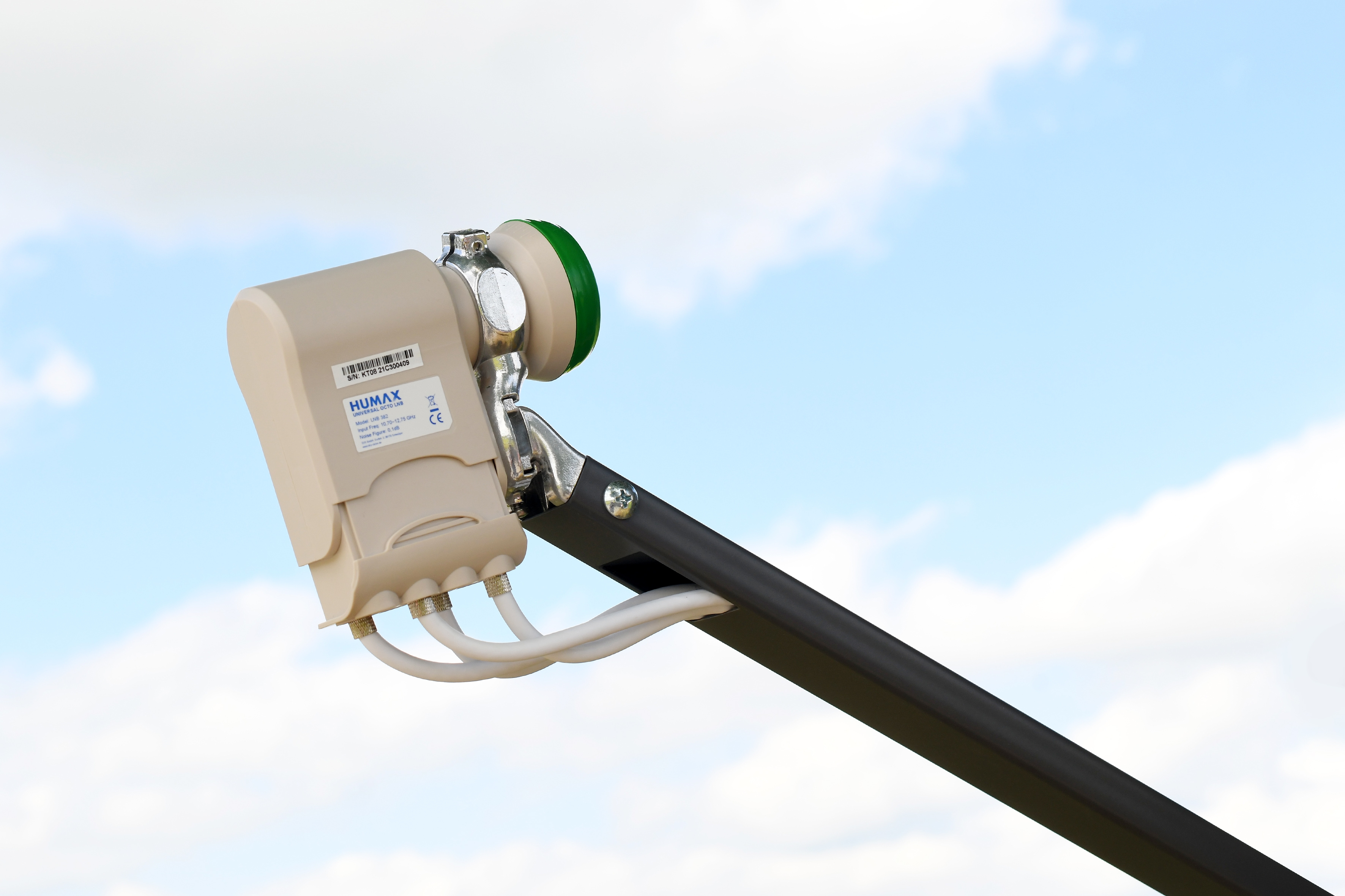 Eine Satellitenschüssel mit weißem und grünem LNB, vor blauem Himmel mit Wolken montiert.