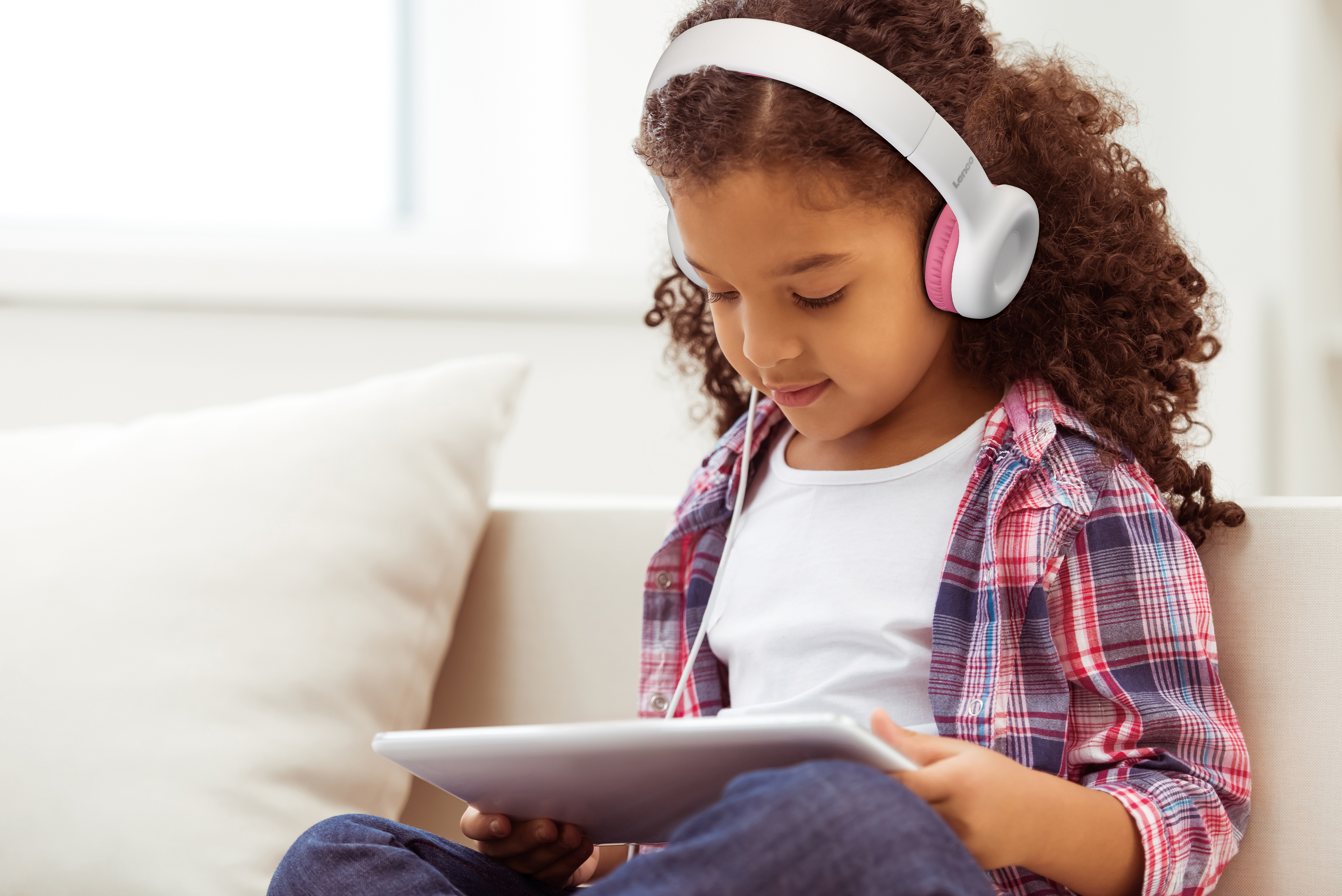 Młoda dziewczyna w różowo-białych słuchawkach, patrząca na tablet.