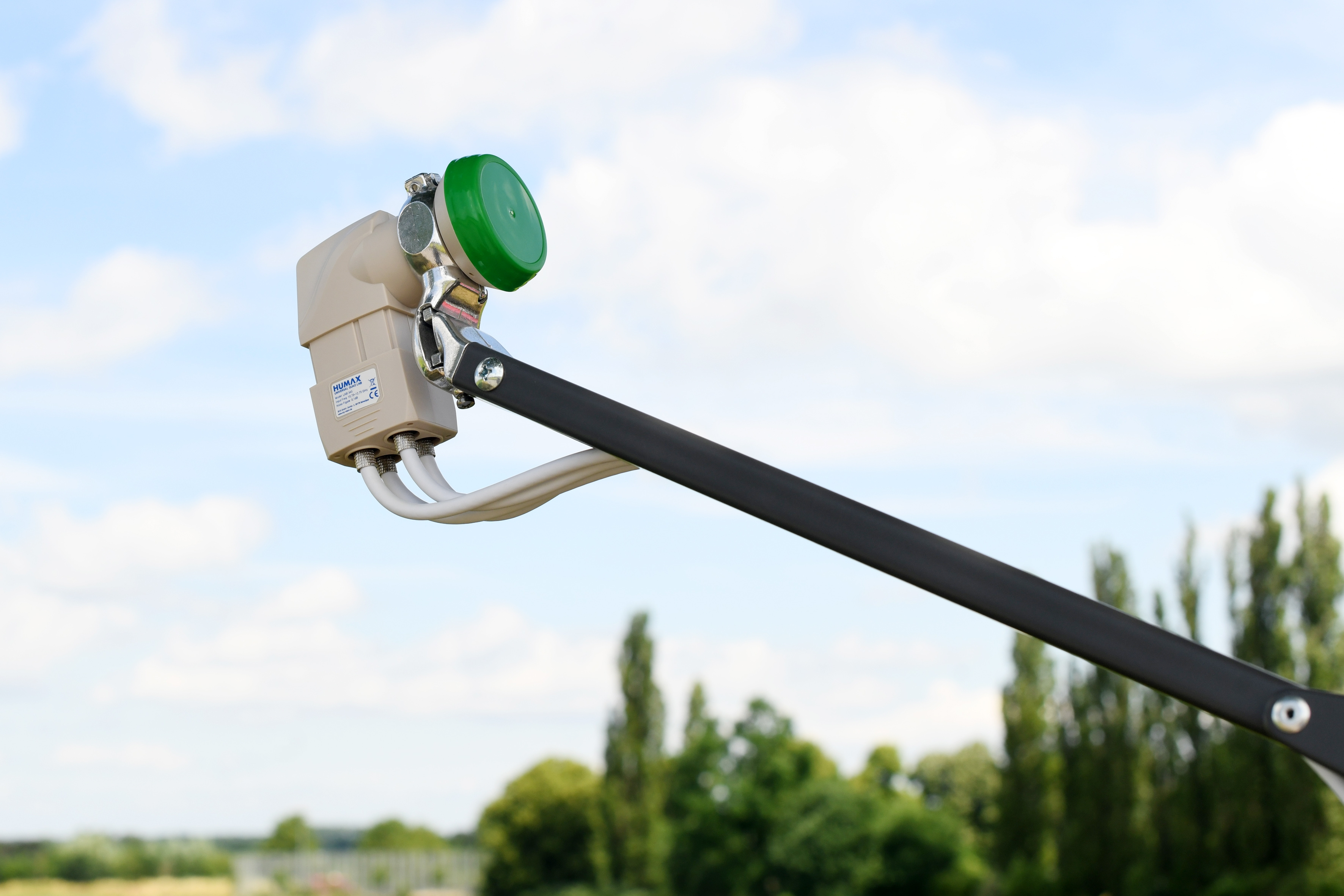 Satellitenschüssel an einem Mast, grüne und beige Komponenten, blauer Himmel im Hintergrund.