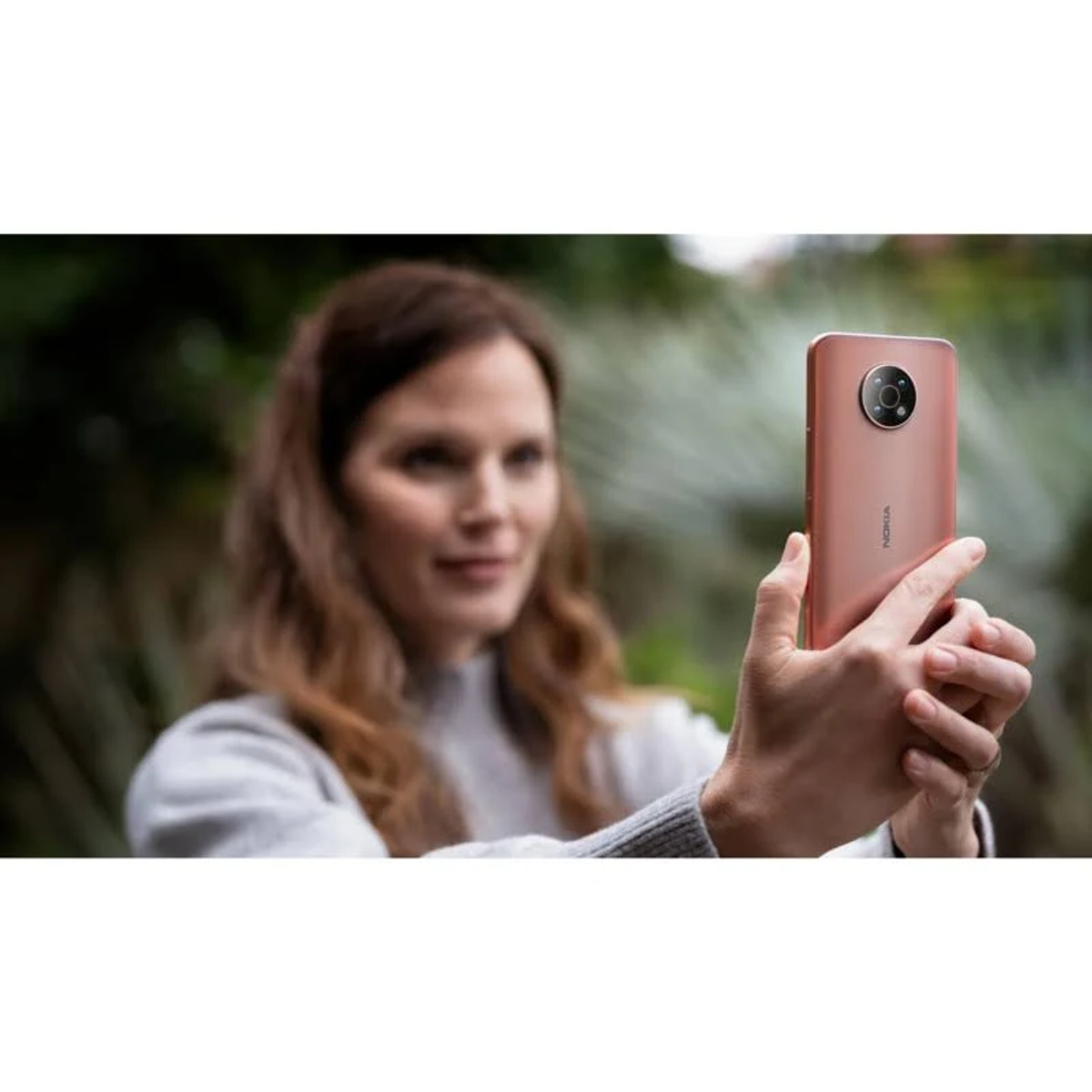 Frau hält ein rosa Telefon und macht ein Foto. Verschwommener Hintergrund.