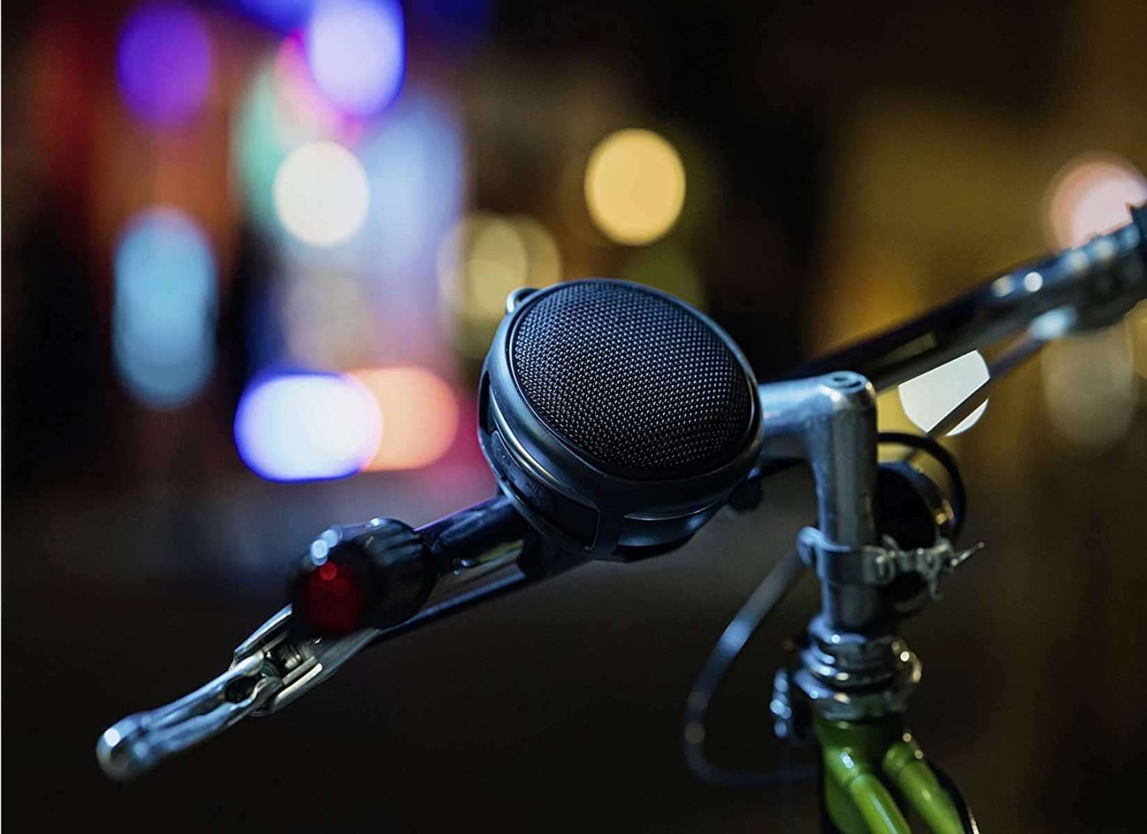 Fahrradlenker mit montiertem Lautsprecher, Nachtszene mit Bokeh-Lichtern.