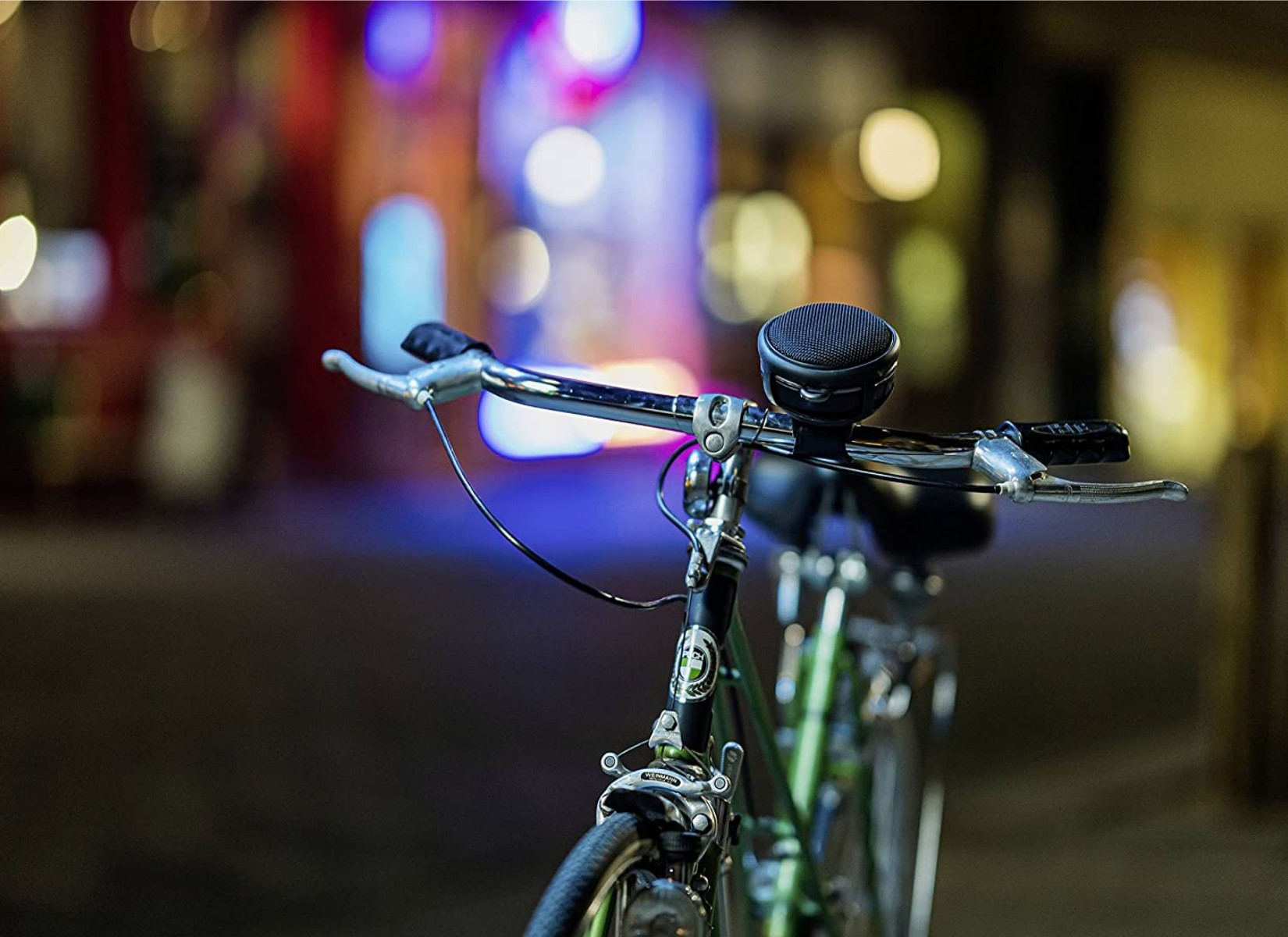 Ein Fahrrad mit einem Lautsprecher am Lenker, in einer verschwommenen urbanen Nachtszene.