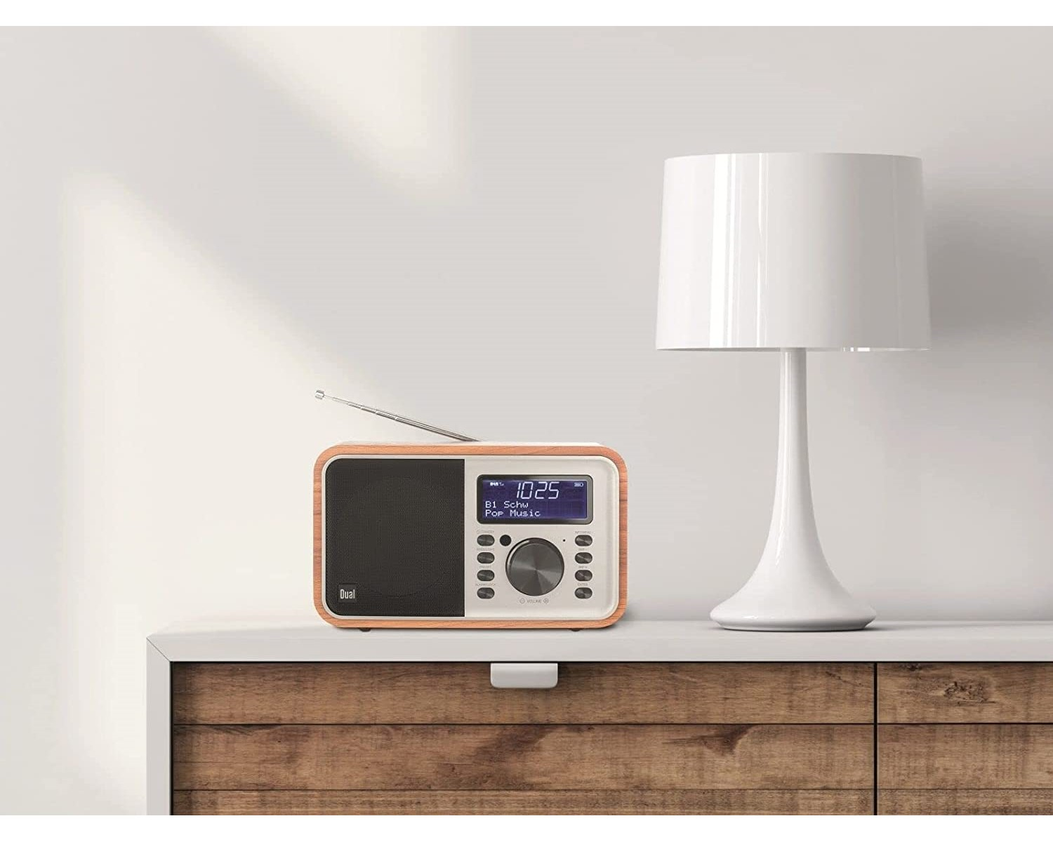 Ein Radio auf einem Holzschrank mit einer weißen Lampe. Der Hintergrund ist eine weiße Wand.