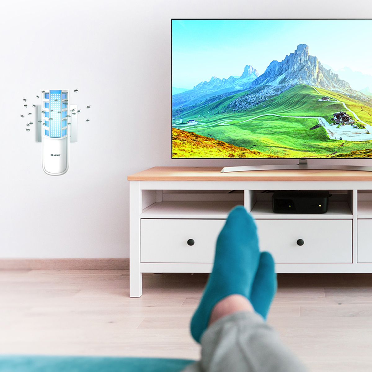 Una persona acostada en un sofá ve la televisión. Un eliminador de insectos montado en la pared a la izquierda.