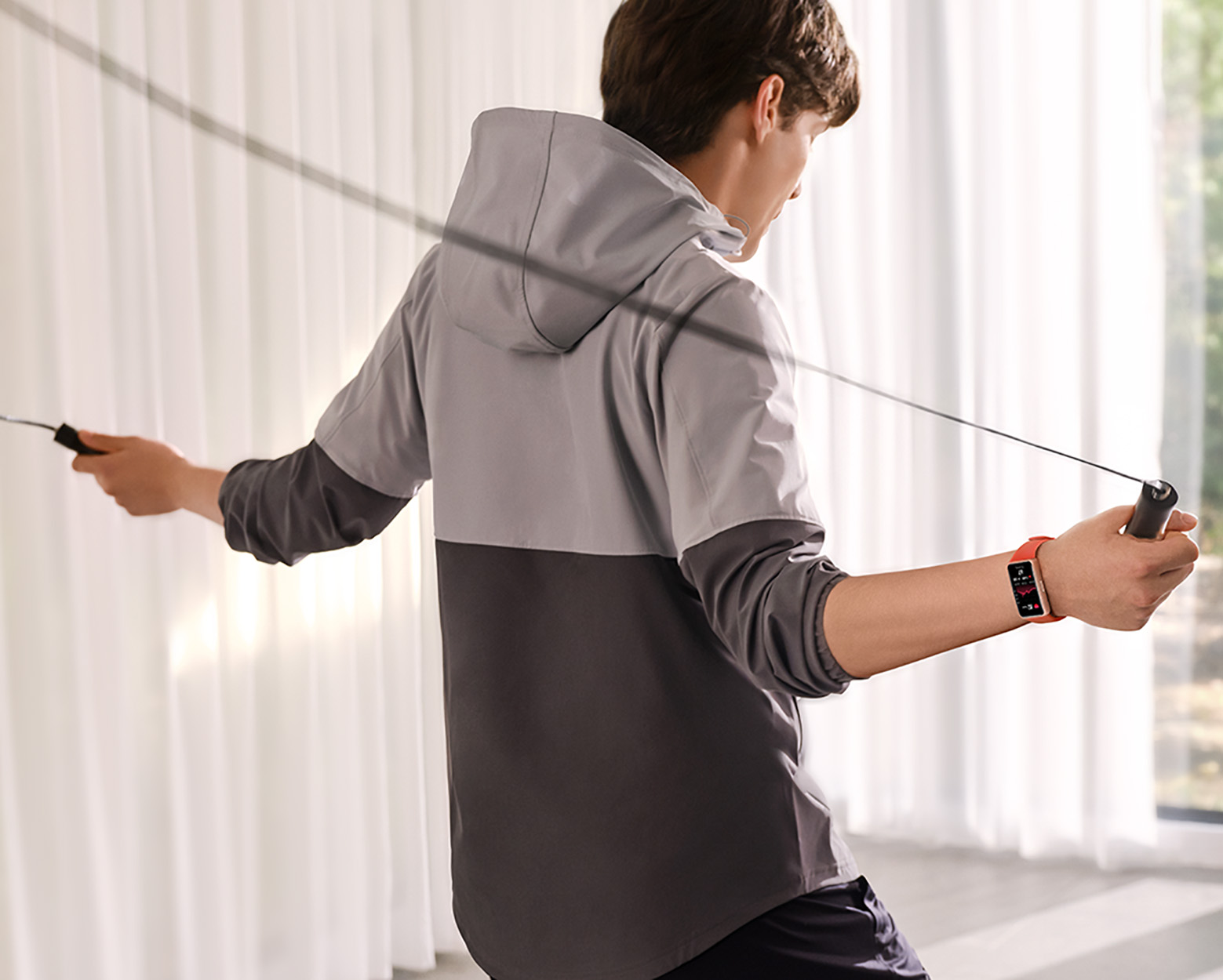 Mężczyzna ćwiczy ze skakanką. Ma na sobie szarą kurtkę i smartwatch.