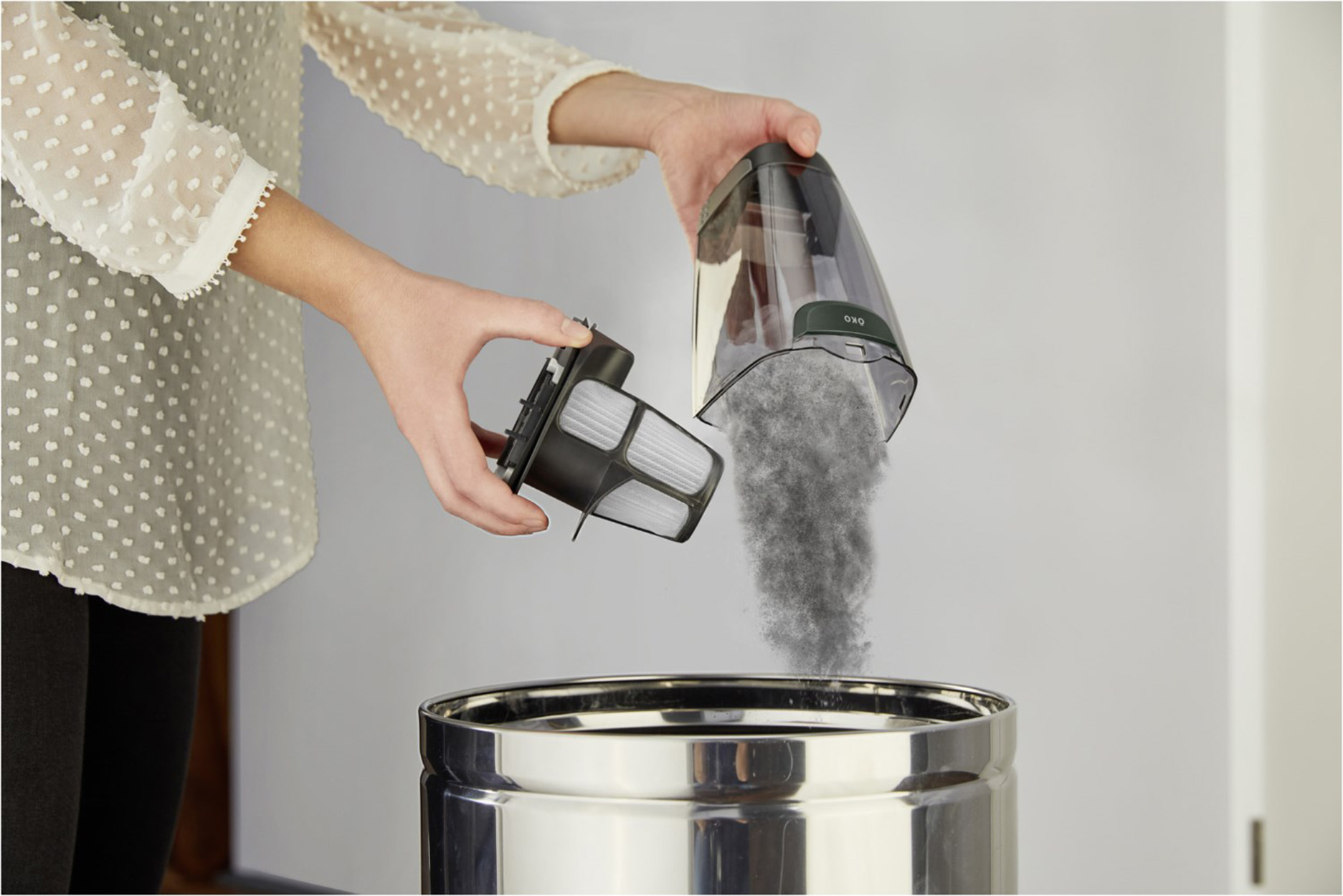 Hände entleeren Staubsaugerfilter in einen Behälter.