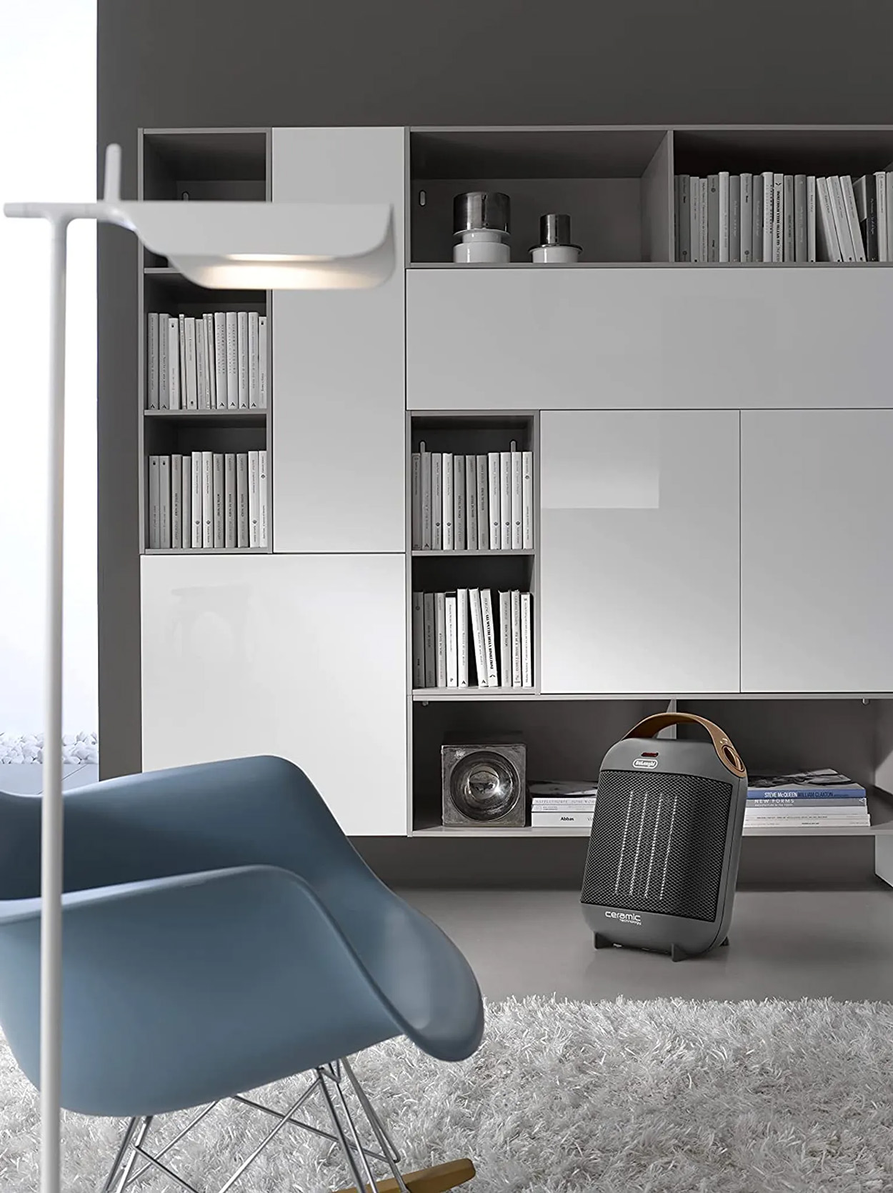 Salon z białymi półkami, niebieskim krzesłem, grzejnikiem i lampą podłogową.