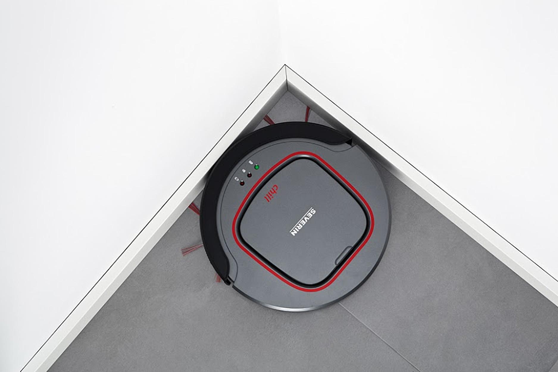 Odkurzacz robot w rogu, szary, z czerwoną obwódką, na tle białych ścian.