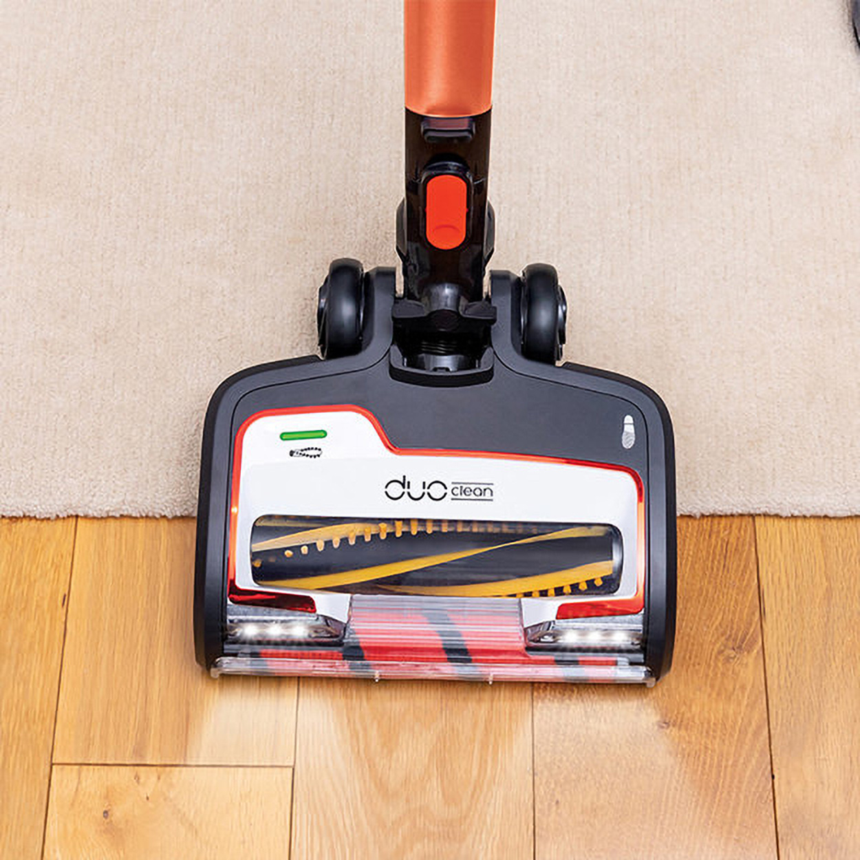 Cabezal de aspiradora negro y rojo sobre suelo de madera y alfombra beige. Etiqueta Duo Clean.
