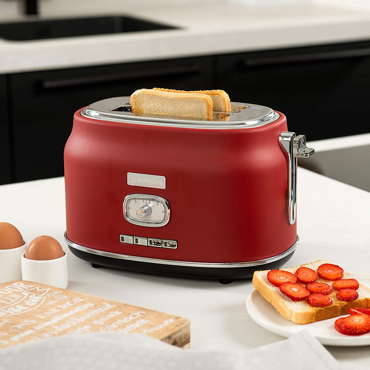 Roter Toaster mit zwei Toastscheiben, Erdbeeren, Eiern und einem Holzbrett.