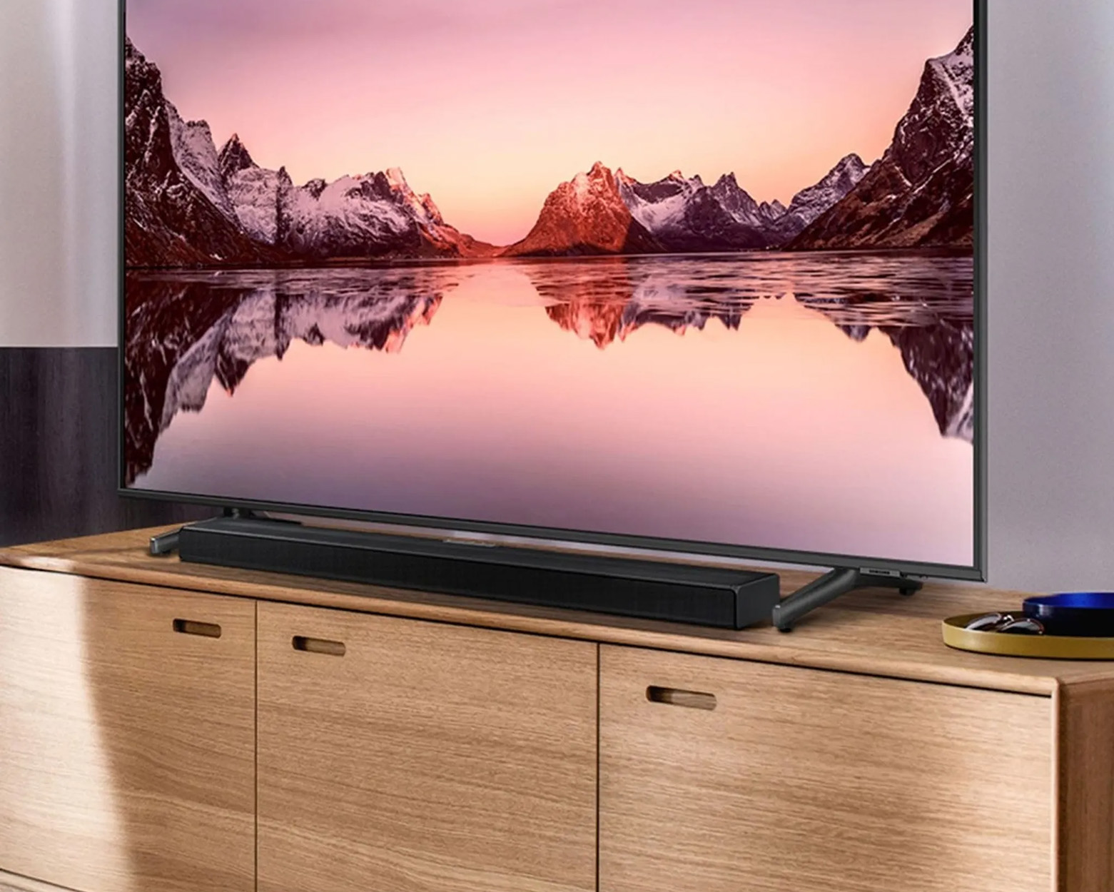 Ein Fernseher auf einem Holzschrank mit Soundbar. Der Fernseher zeigt eine Landschaft mit Bergen.
