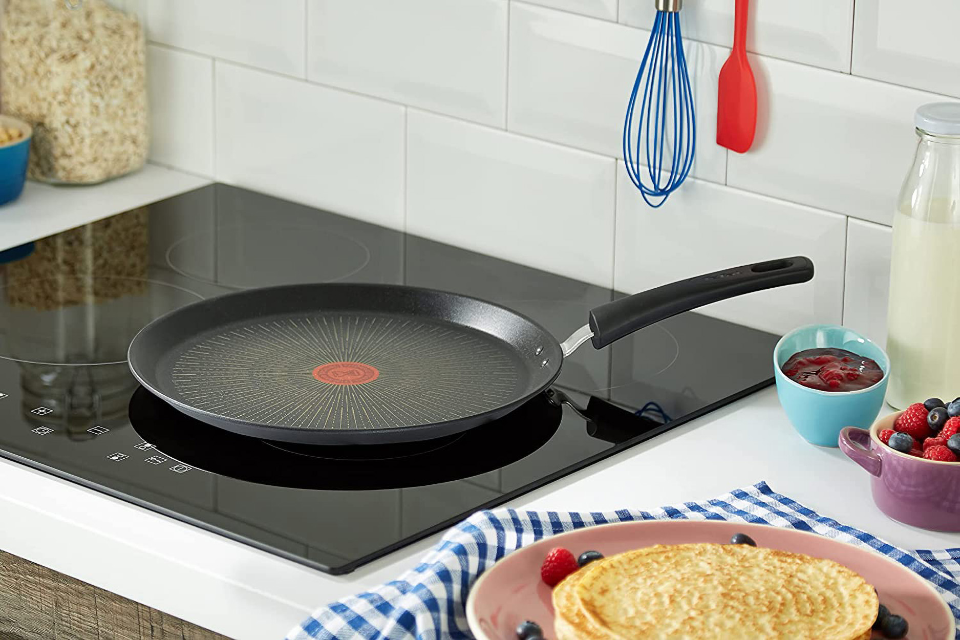 Czarna patelnia na czarnej płycie kuchennej. Naleśniki i dodatki są w pobliżu. Ustawienia kuchni, dobrze oświetlone.