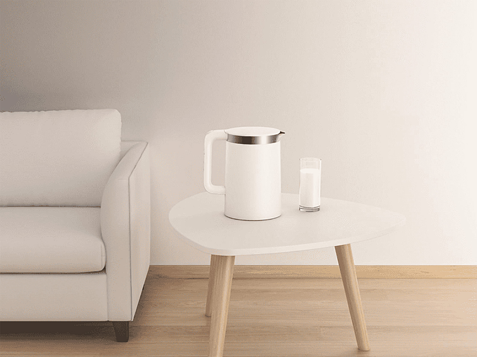 Witte elektrische waterkoker en glas melk op een witte tafel, naast een witte bank.