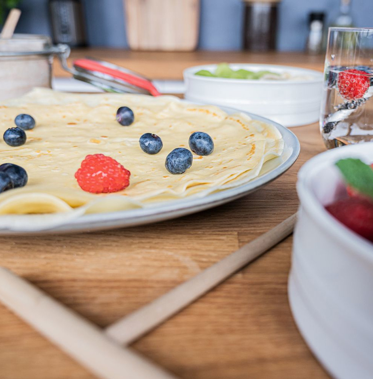 Naleśniki na talerzu z jagodami i maliną. Widoczne są inne składniki i przedmioty.