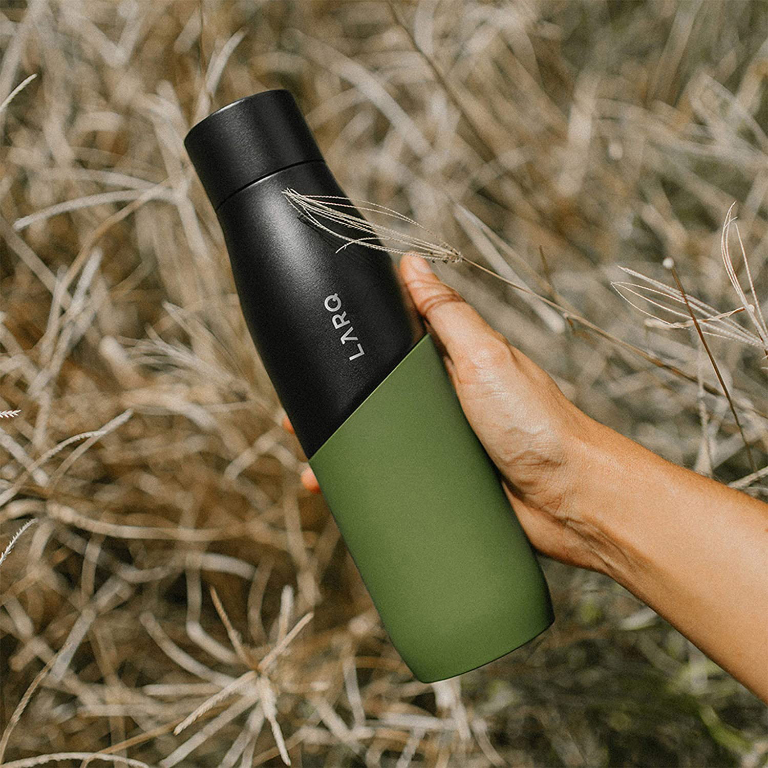 Eine schwarz-olivgrüne Wasserflasche wird von einer Hand gehalten. Die Flasche trägt die Aufschrift LARQ.