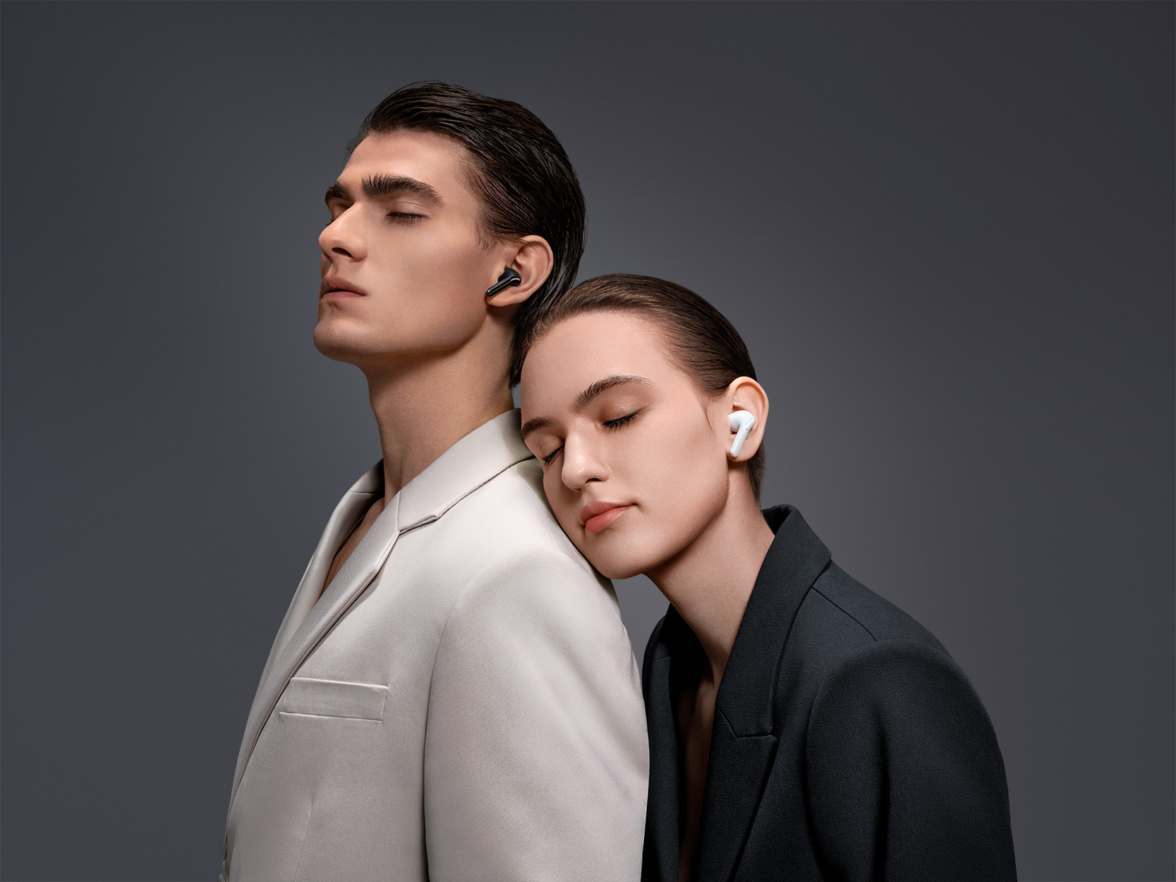 Un hombre y una mujer con los ojos cerrados usando auriculares, fondo gris.
