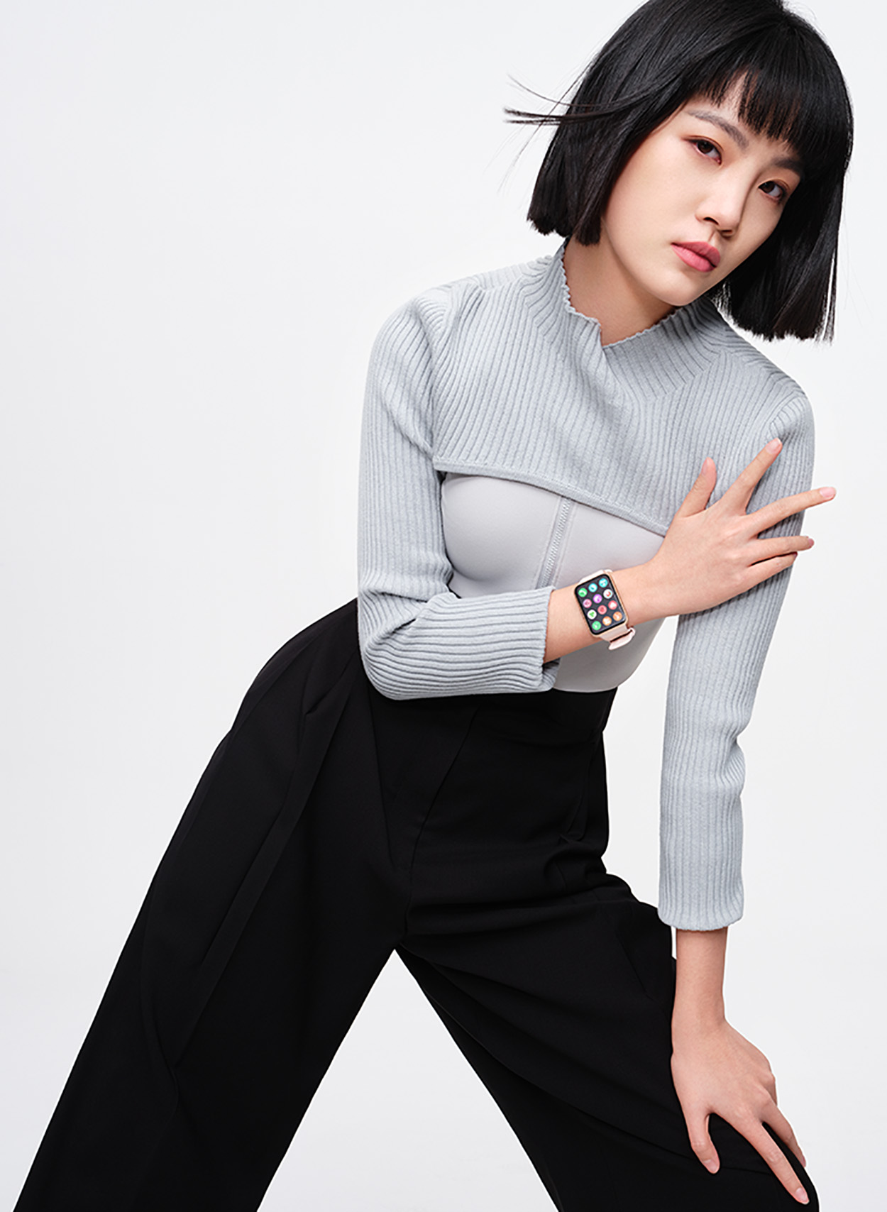 Una mujer con top celeste y pantalón negro lleva un reloj inteligente y posa.