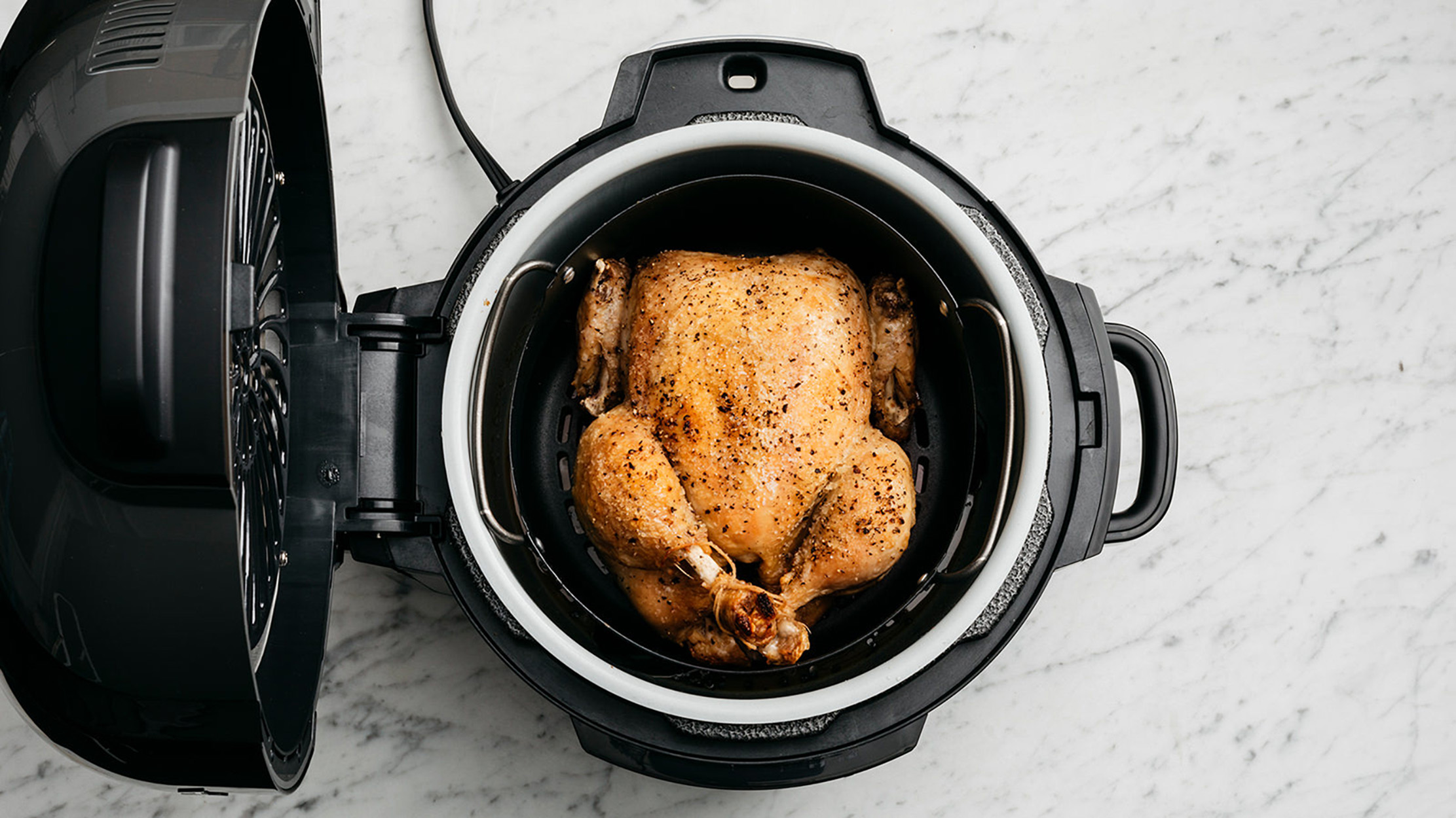 Pollo intero arrosto all'interno di una friggitrice ad aria, coperchio aperto. Il pollo è dorato e condito.