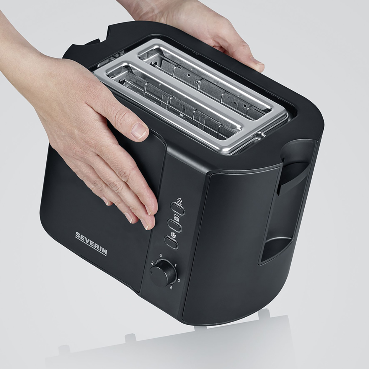Hände halten einen schwarzen Toaster. Silberne Schlitze, schwarze Knöpfe. Heller Hintergrund.