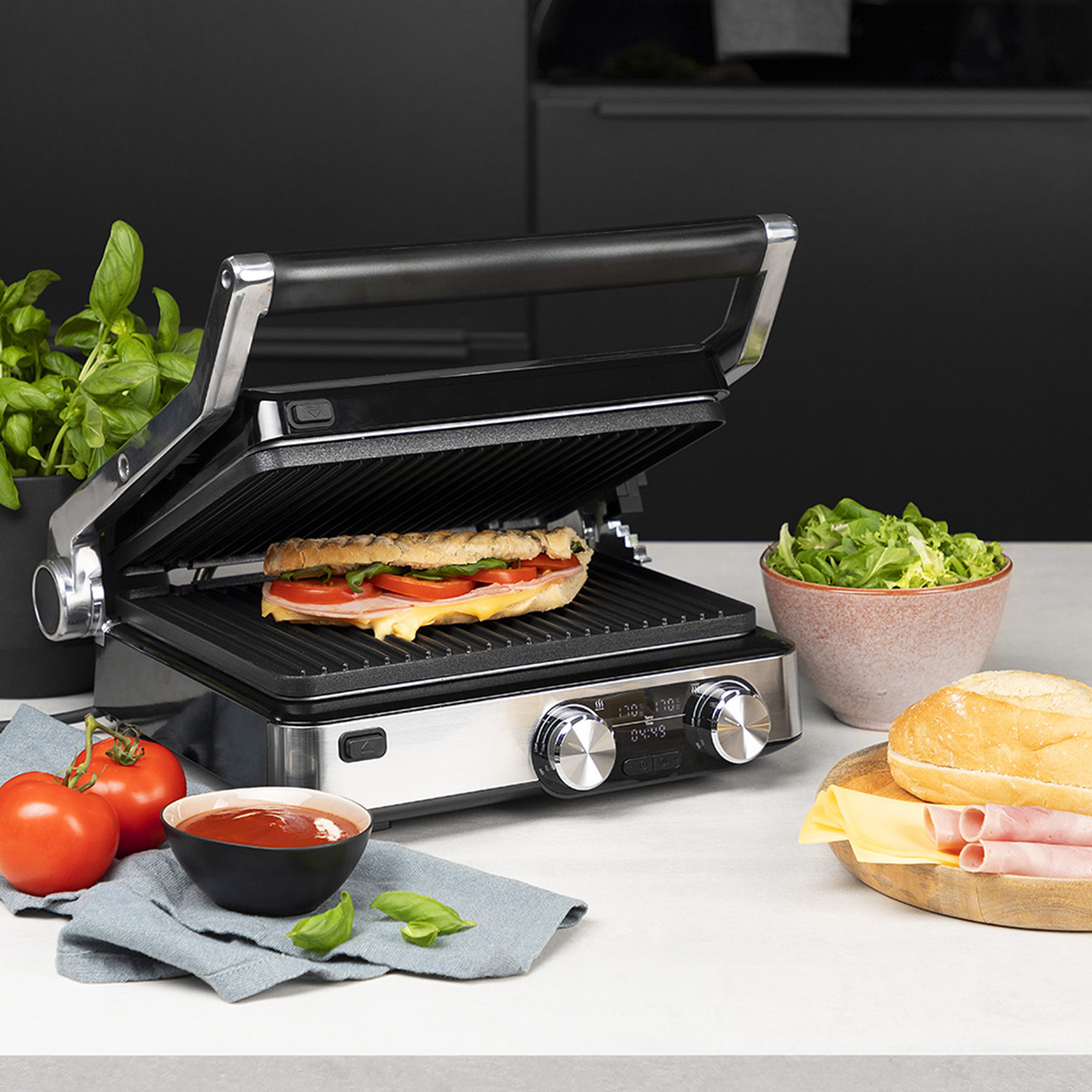Ein Sandwich auf einem Grill, Tomaten, Salat und Brot auf einer Theke mit Basilikum.