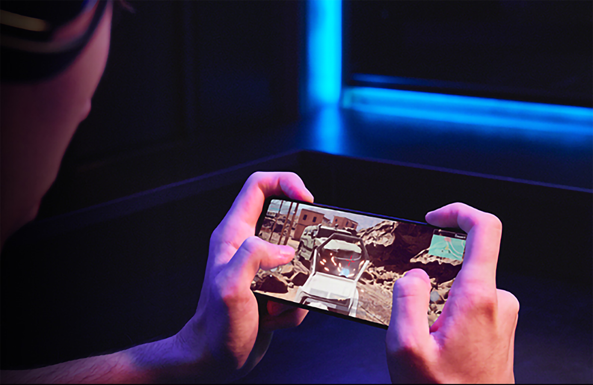 Osoba trzyma telefon z grą wideo, w tle niebieskie światło.