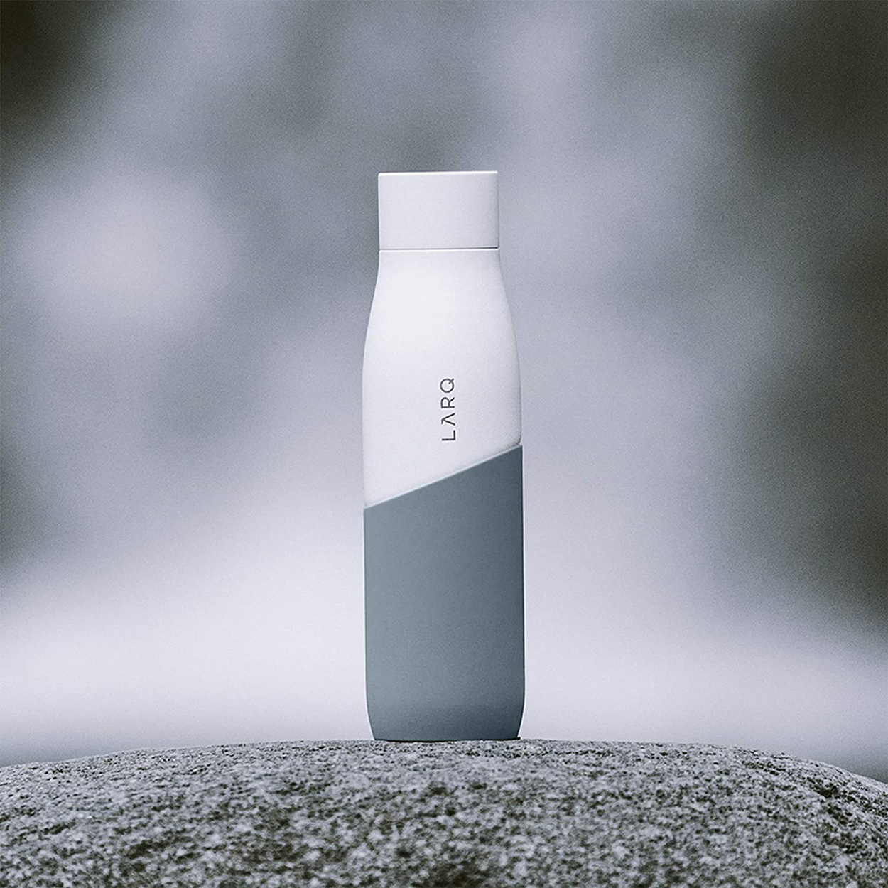 Weiße und graue Larq Wasserflasche auf einer Steinoberfläche. Die Flasche steht vertikal.
