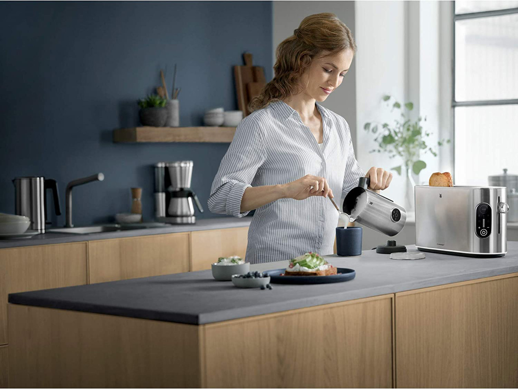 Kobieta nalewa z czajnika do kubka. Kuchnia z tosterem i jedzeniem.