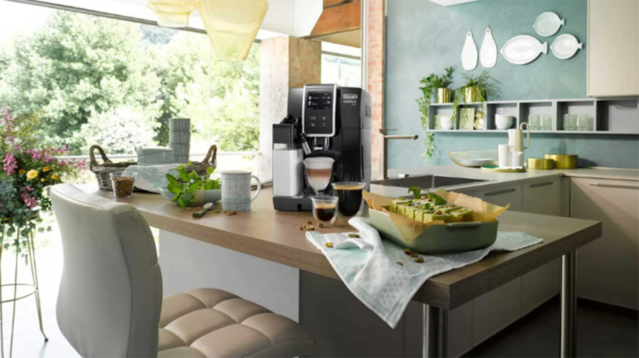 Küchenszene mit Kaffeemaschine, Holztisch, und verschiedenen Essens- und Dekorationselementen. Fenster im Hintergrund.